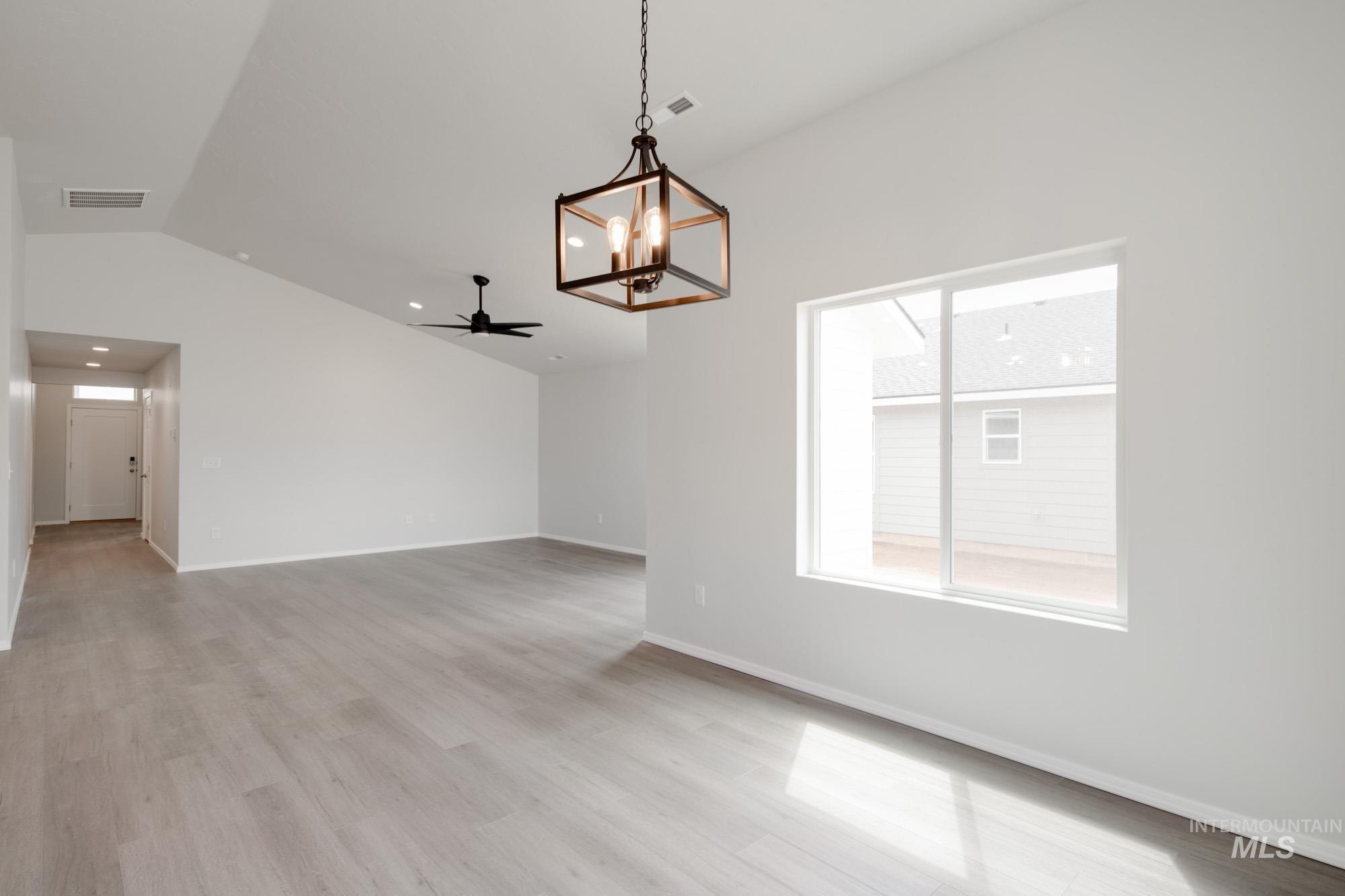 Unfurnished room featuring a chandelier, lofted ceiling, a ceiling fan, and light wood-style floors