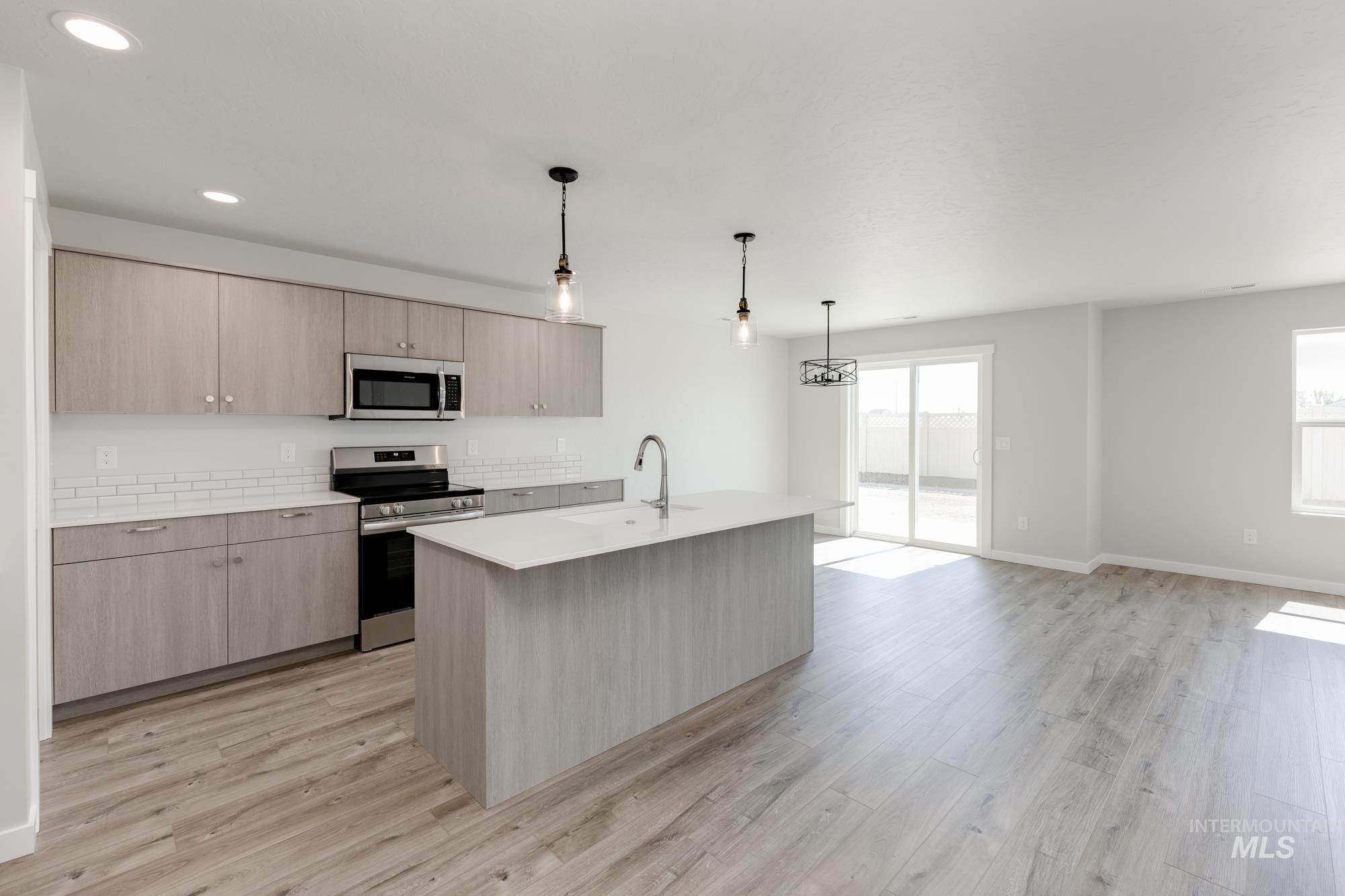 Kitchen featuring stainless steel appliances, decorative light fixtures, light brown cabinetry, light wood finished floors, and recessed lighting