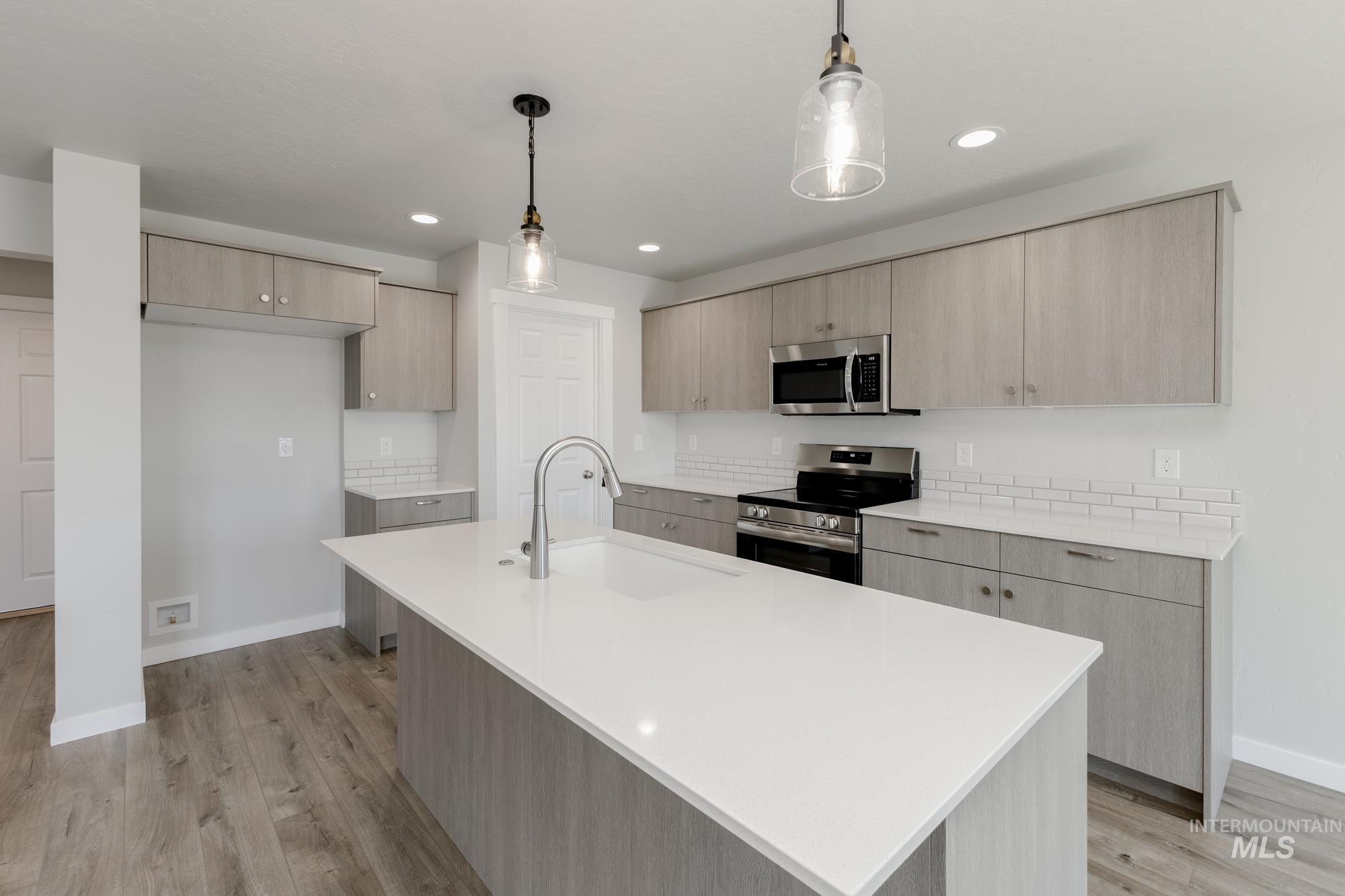 Kitchen with light brown cabinetry, modern cabinets, appliances with stainless steel finishes, hanging light fixtures, and light wood-style flooring