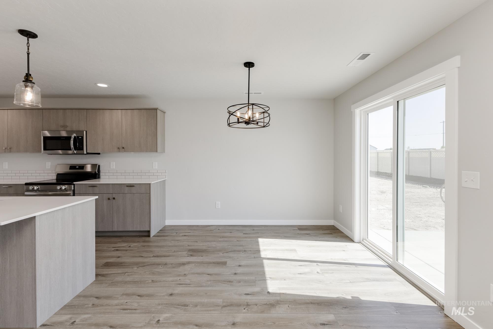Kitchen featuring appliances with stainless steel finishes, pendant lighting, a chandelier, light wood-style floors, and modern cabinets