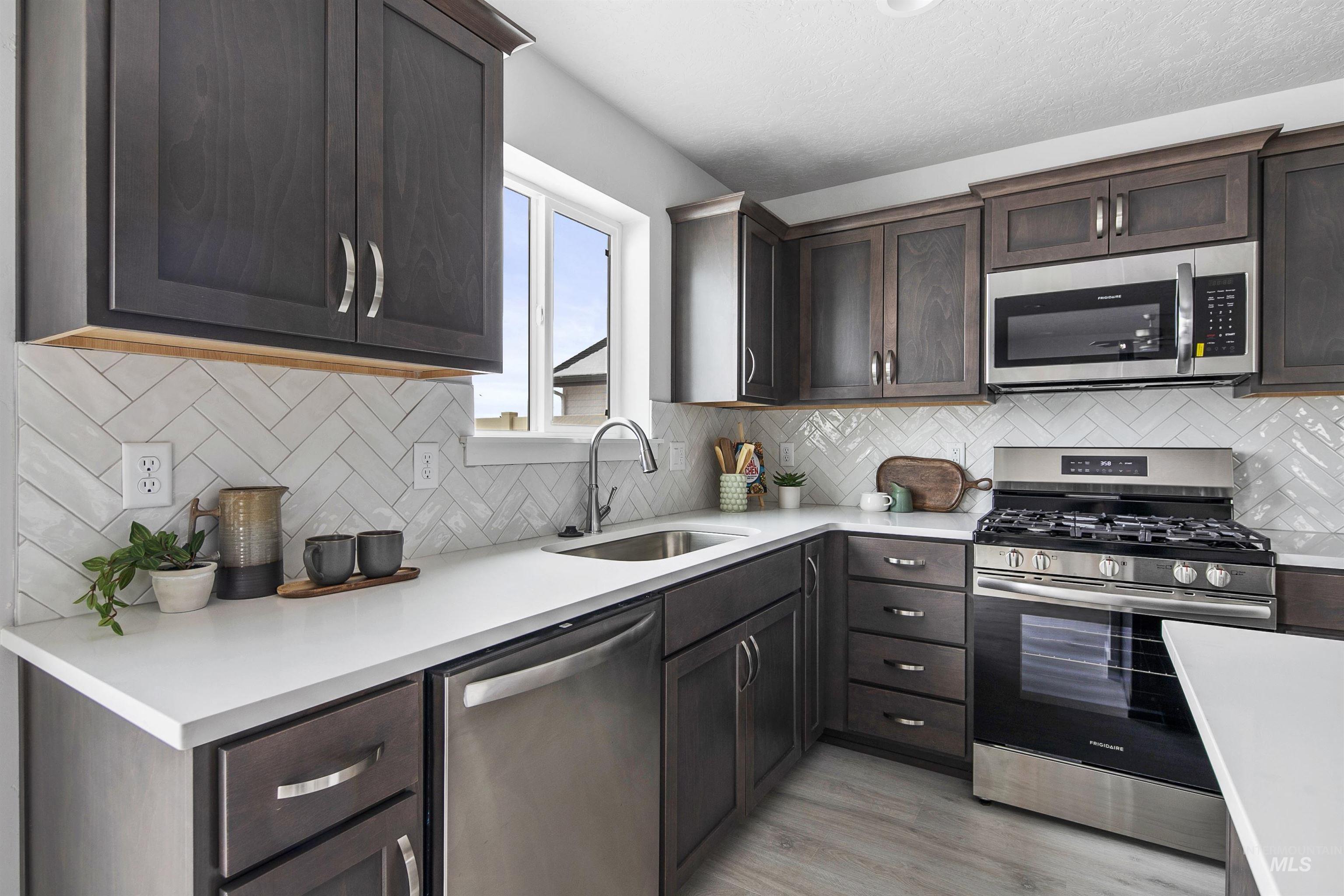 Kitchen featuring stainless steel appliances, dark brown cabinets, light wood-style floors, backsplash, and light stone countertops