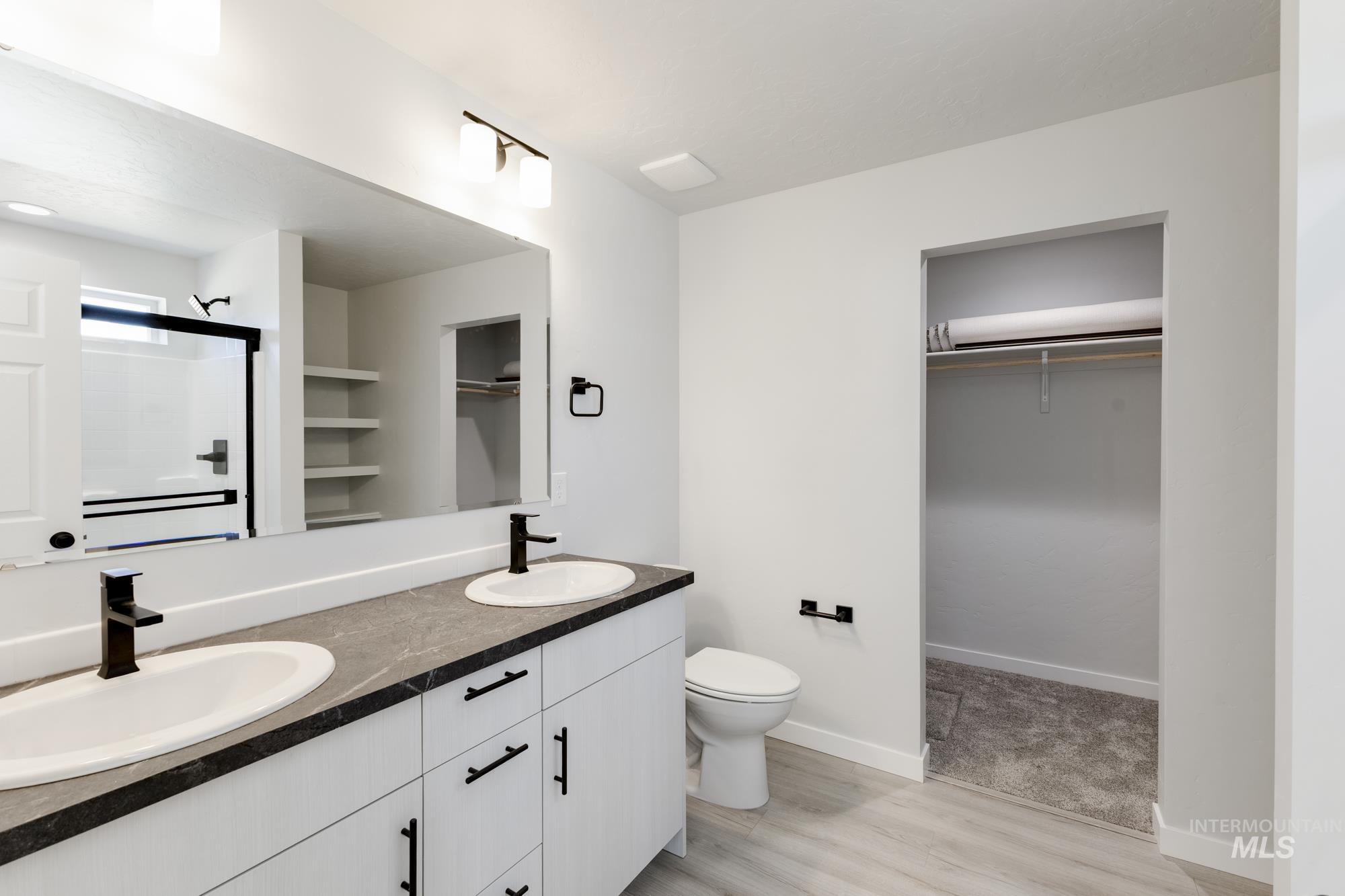 Bathroom with a spacious closet, an enclosed shower, double vanity, and light wood-style flooring