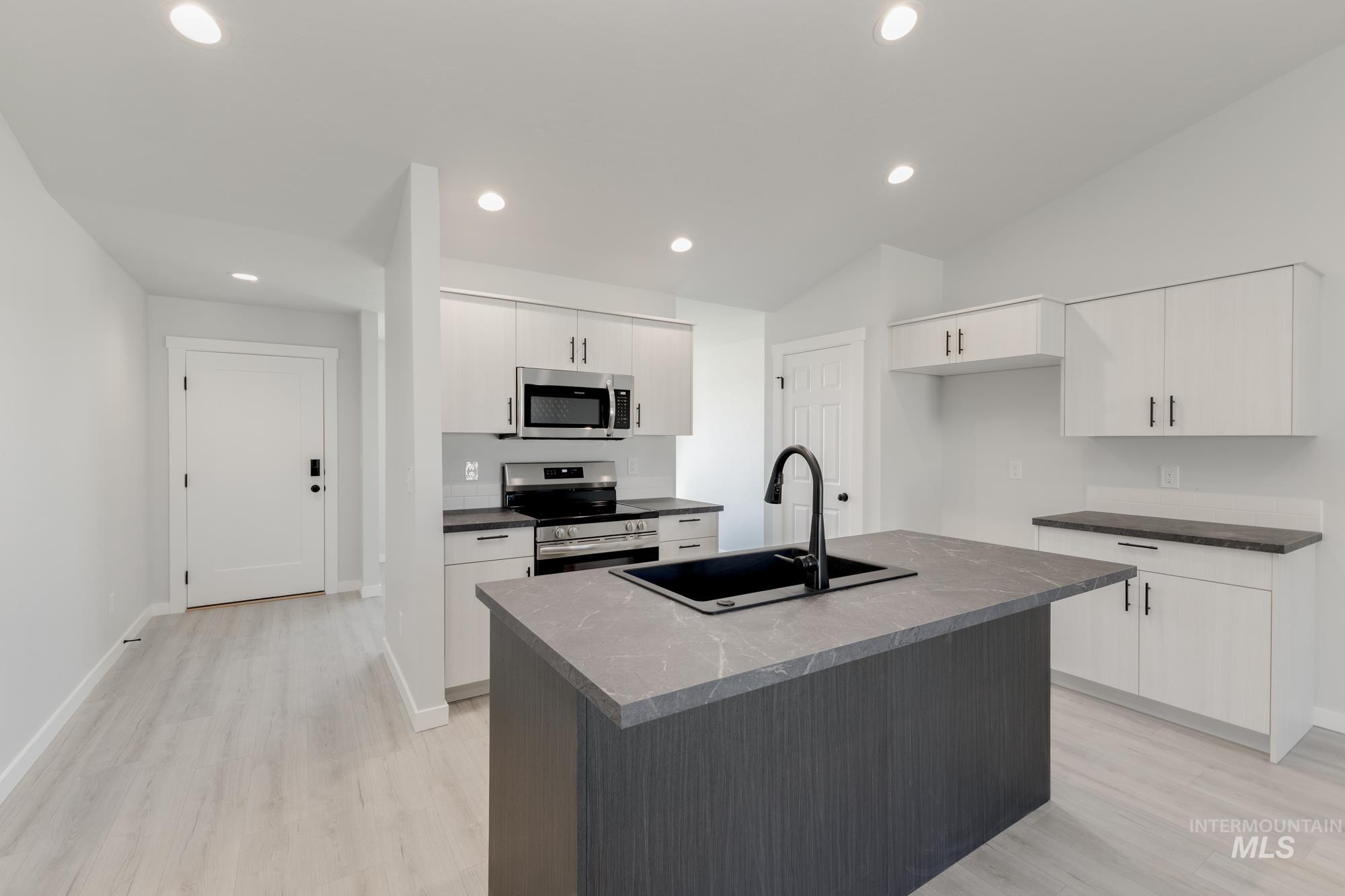 Kitchen with stainless steel appliances, a center island with sink, light wood-style flooring, white cabinetry, and recessed lighting