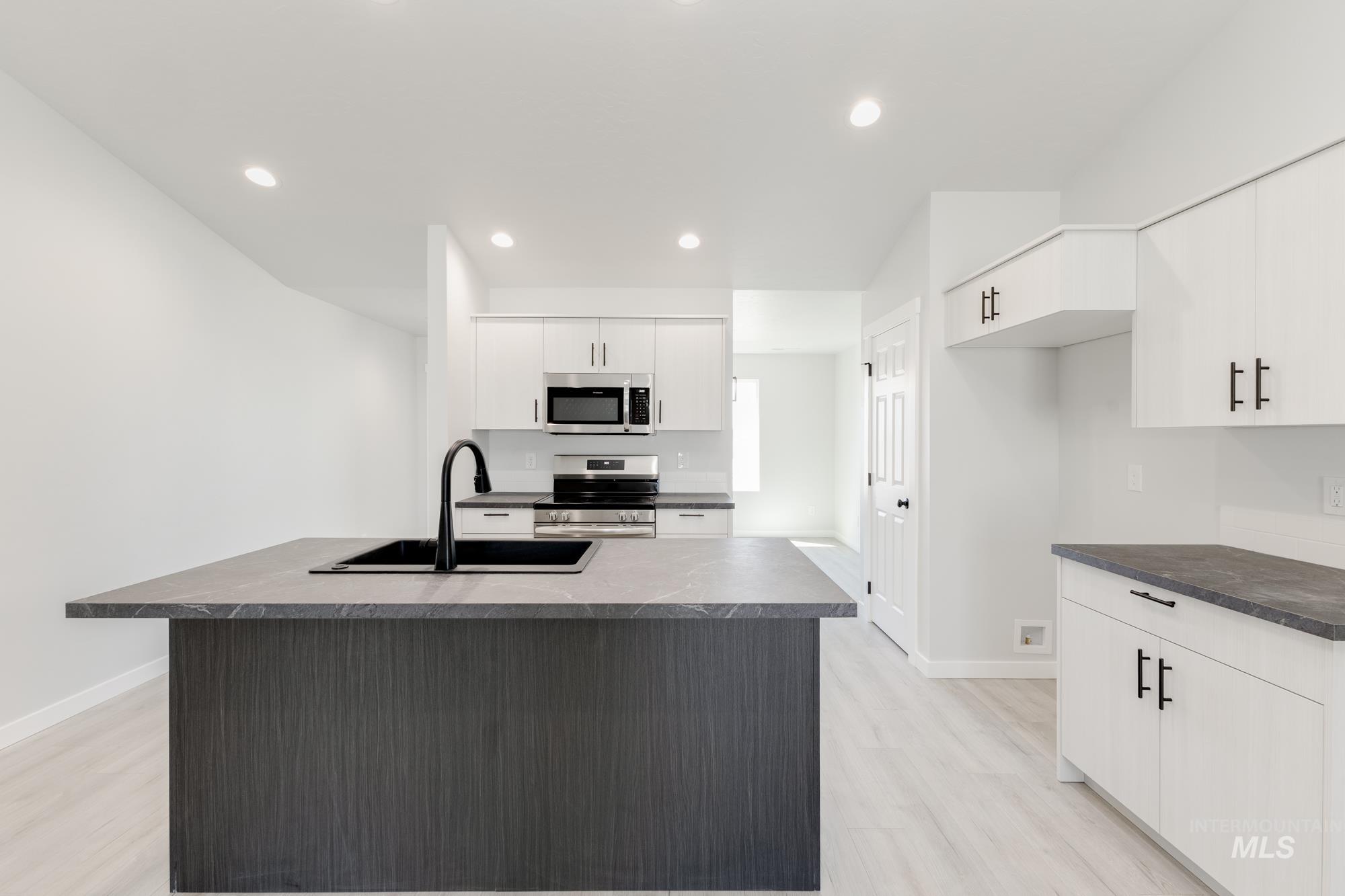 Kitchen with an island with sink, appliances with stainless steel finishes, recessed lighting, light wood-style floors, and white cabinets