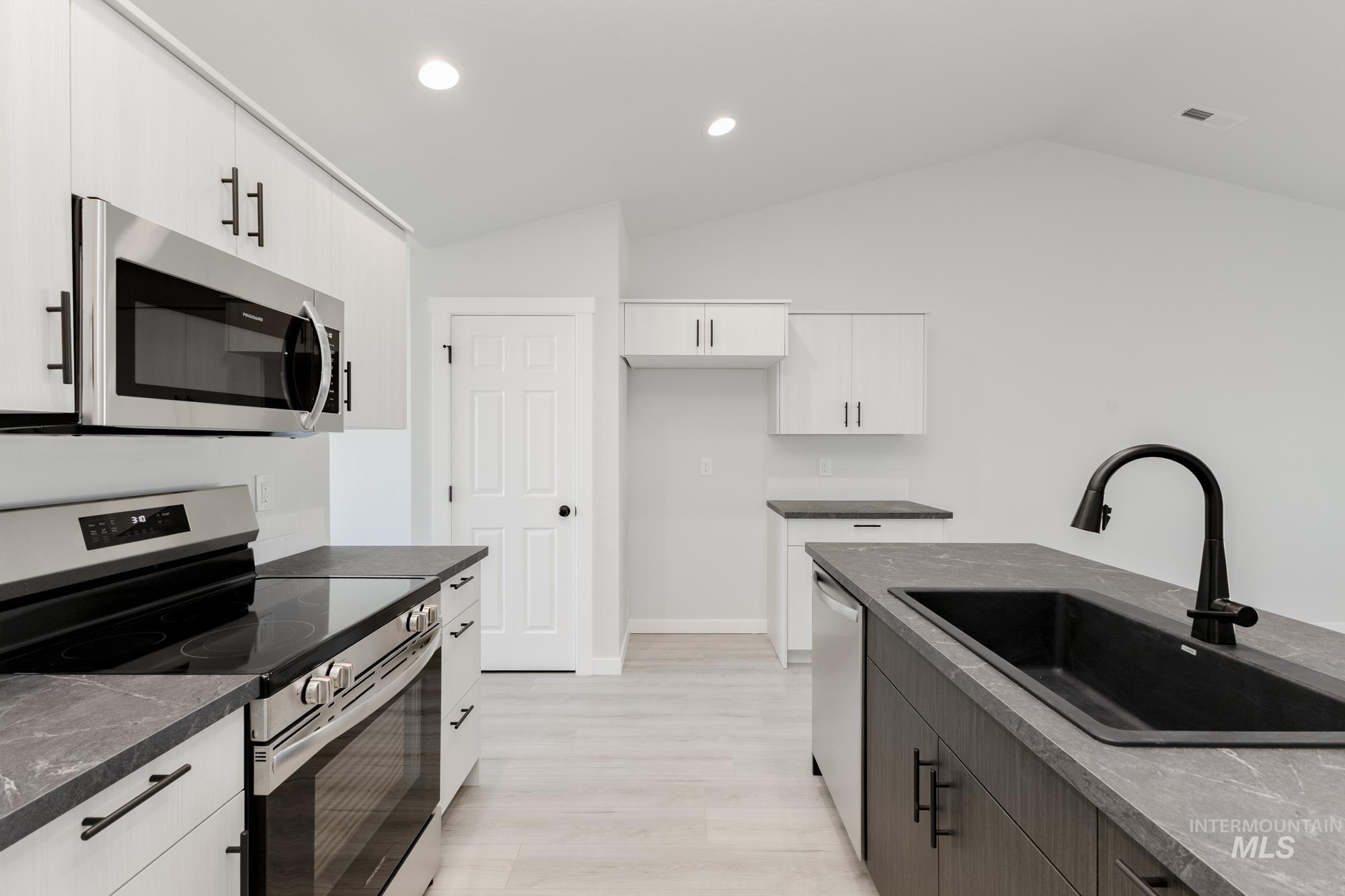 Kitchen with appliances with stainless steel finishes, recessed lighting, dark stone countertops, white cabinets, and vaulted ceiling