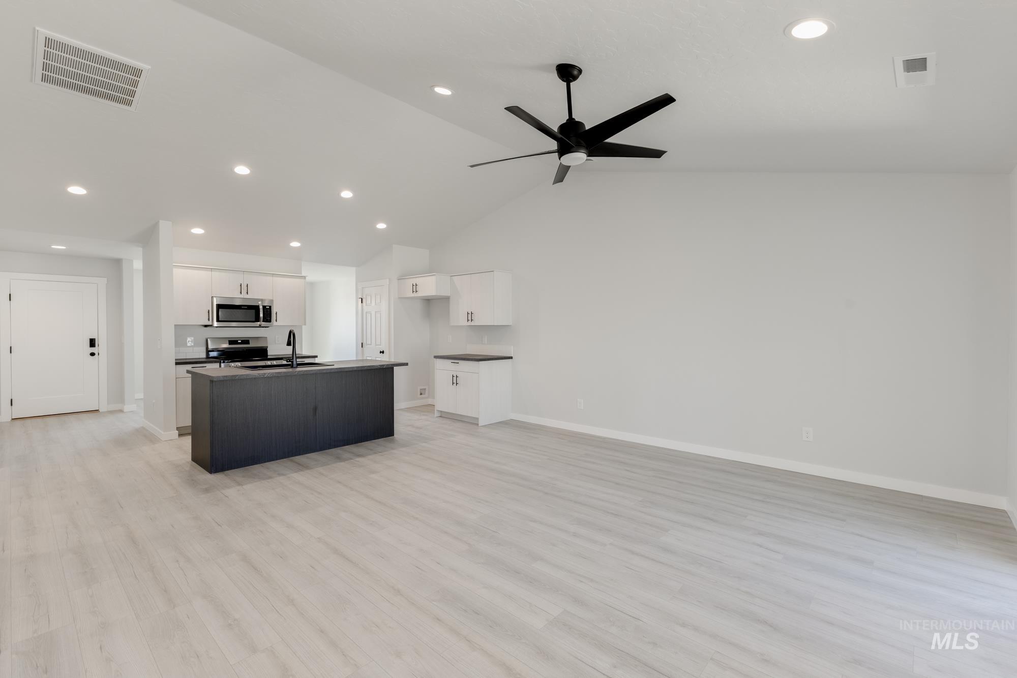 Kitchen with open floor plan, dark countertops, white cabinetry, recessed lighting, and light wood-style floors