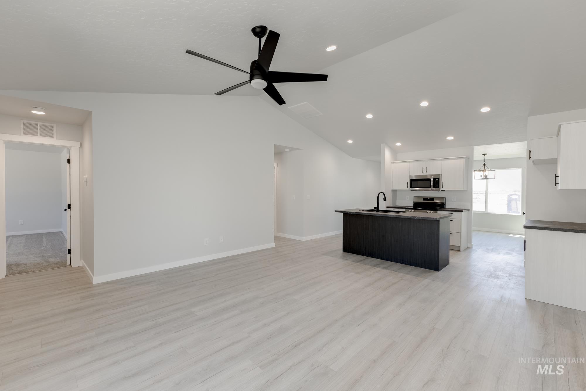 Unfurnished living room with vaulted ceiling, light wood-style flooring, recessed lighting, ceiling fan, and a chandelier
