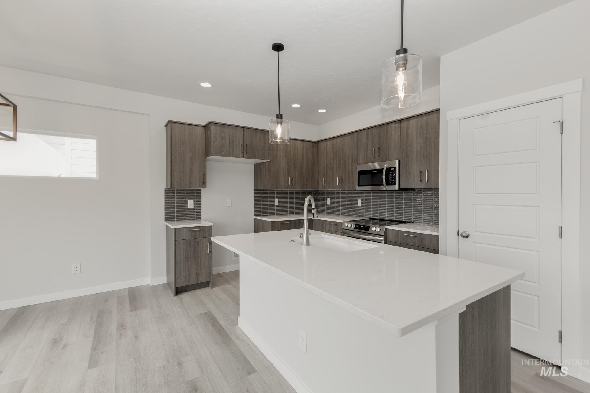 Kitchen with modern cabinets, light stone counters, backsplash, light wood-type flooring, and appliances with stainless steel finishes