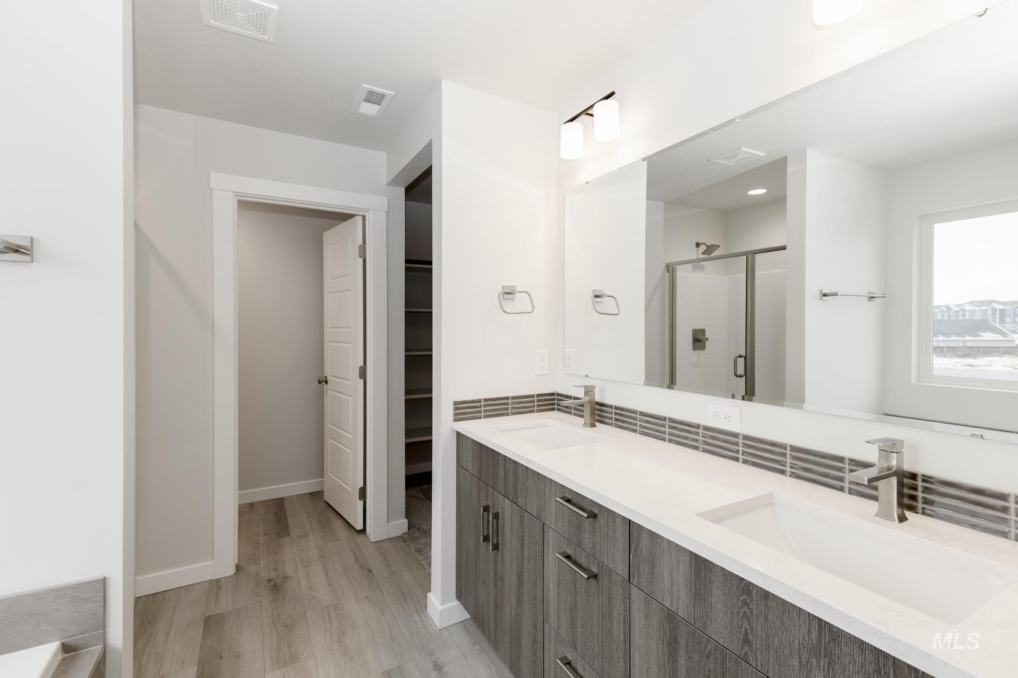 Full bath with double vanity, a shower stall, light wood finished floors, and a walk in closet