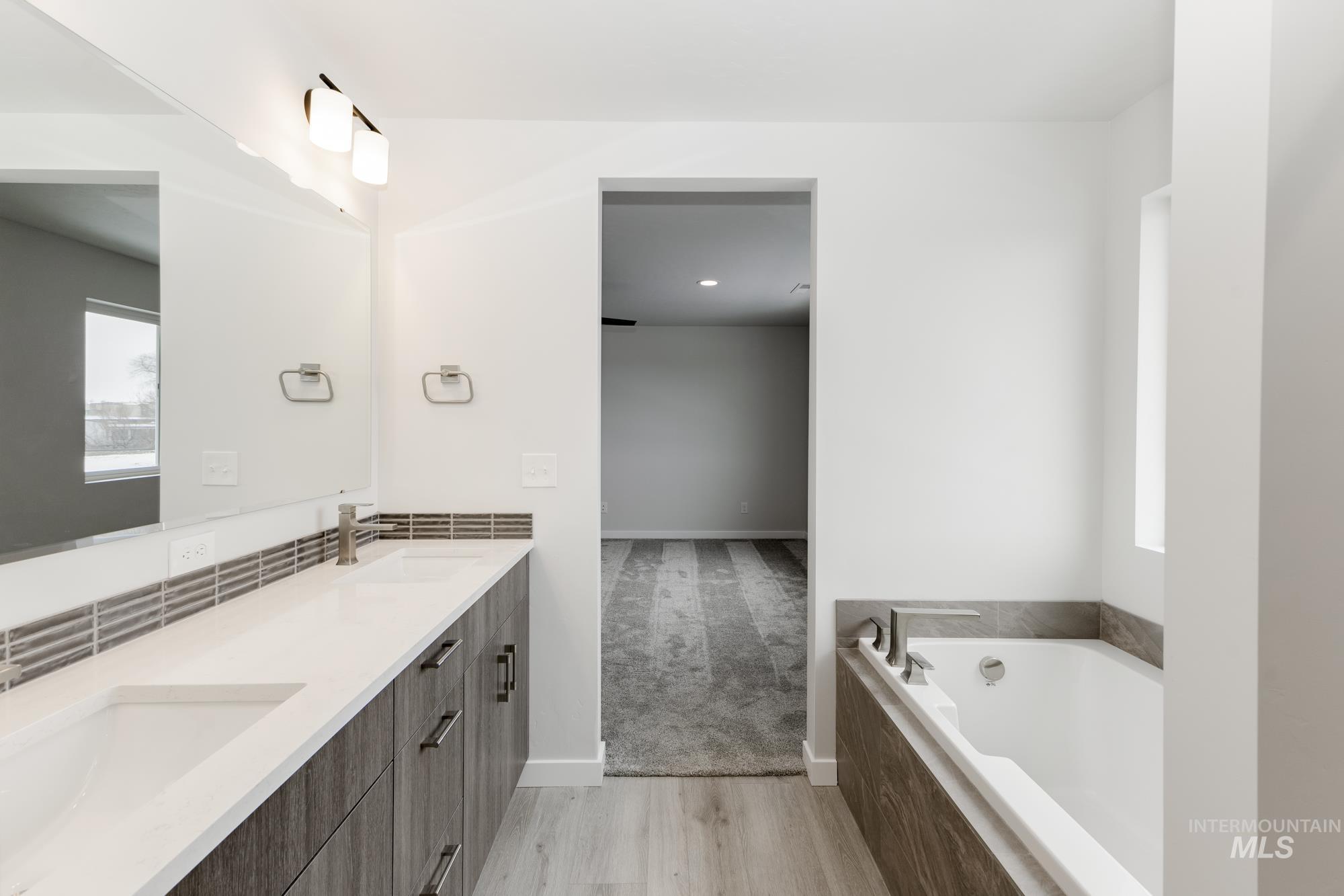 Bathroom featuring double vanity, a bath, and light wood-type flooring