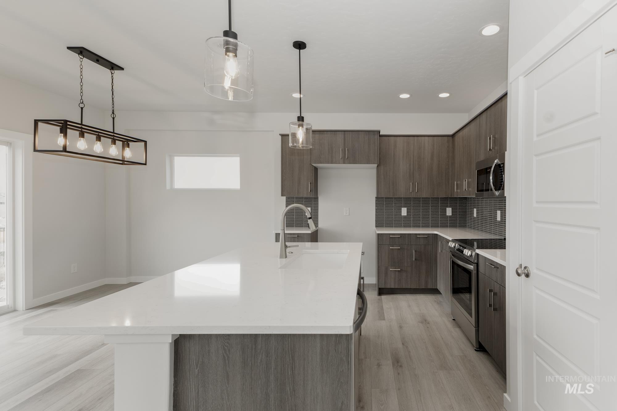 Kitchen featuring backsplash, modern cabinets, appliances with stainless steel finishes, pendant lighting, and light wood-type flooring