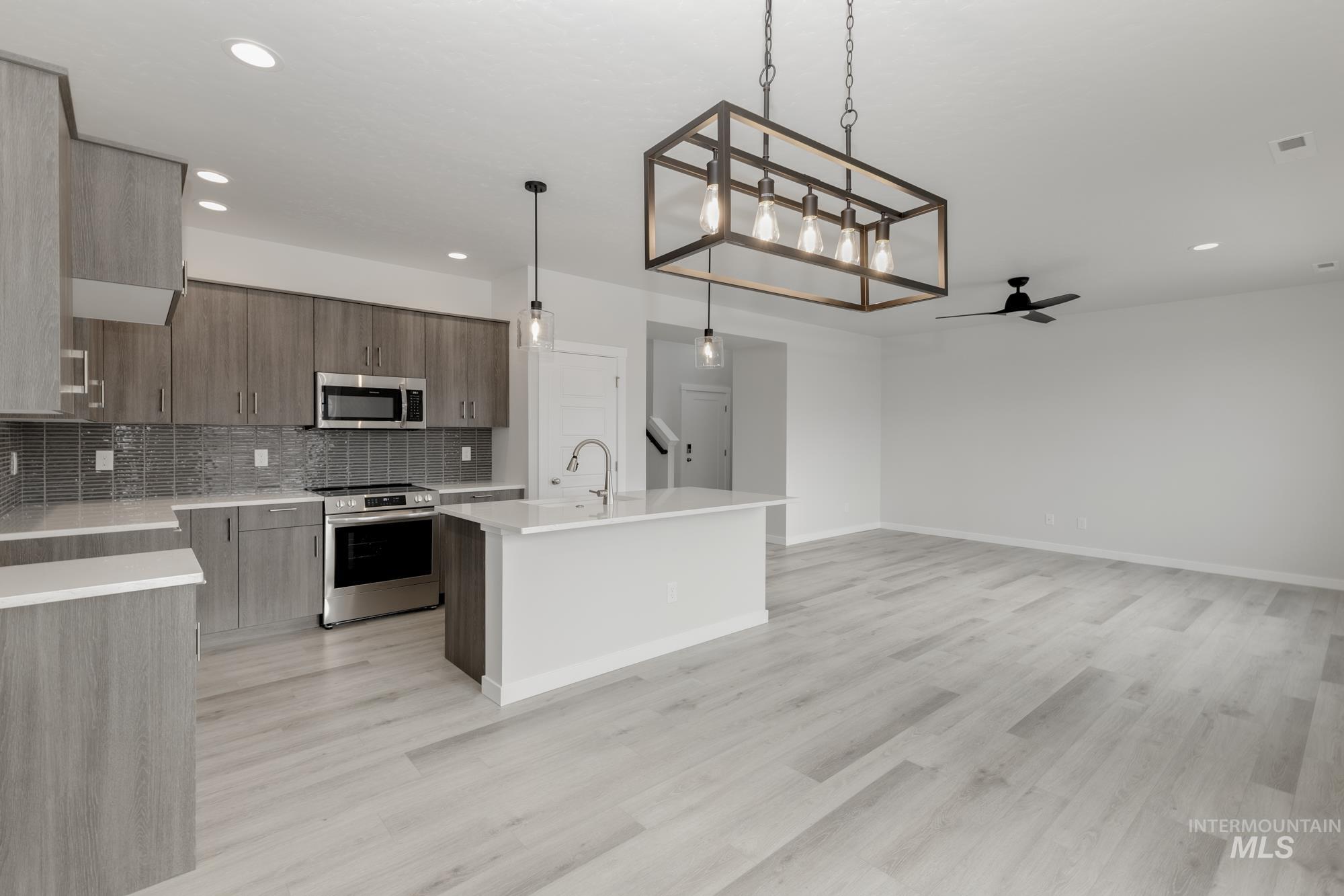 Kitchen featuring decorative backsplash, appliances with stainless steel finishes, an island with sink, light stone counters, and decorative light fixtures