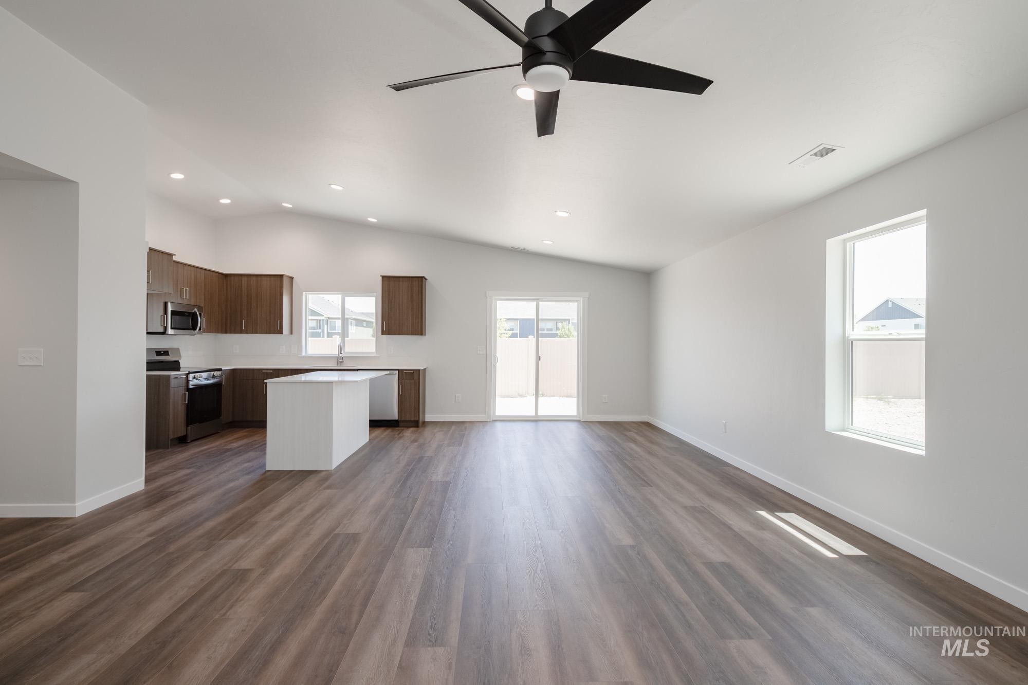 Kitchen featuring open floor plan, light countertops, stainless steel appliances, dark wood-style flooring, and a center island