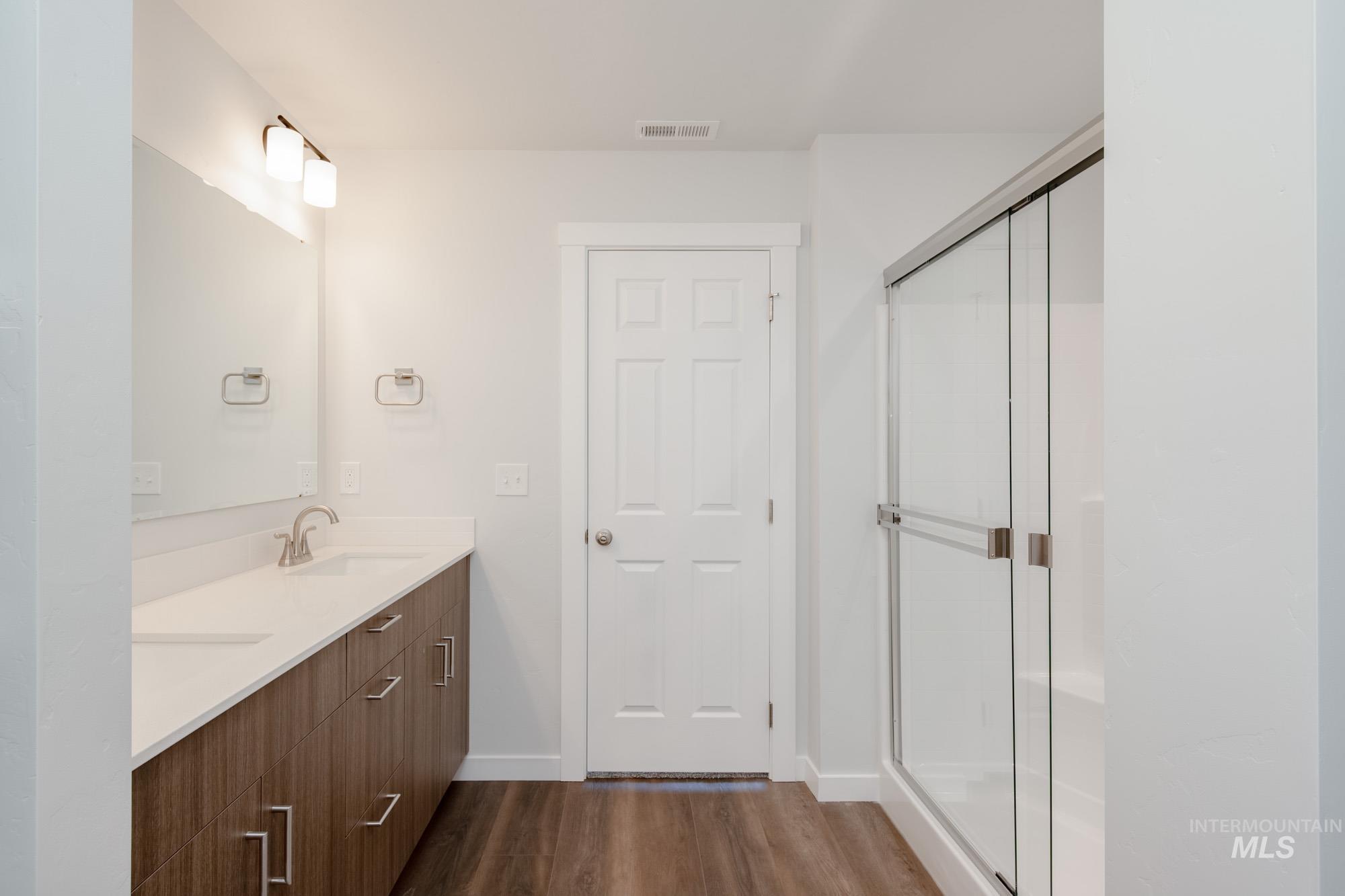 Full bath with dark wood-type flooring, a stall shower, and double vanity