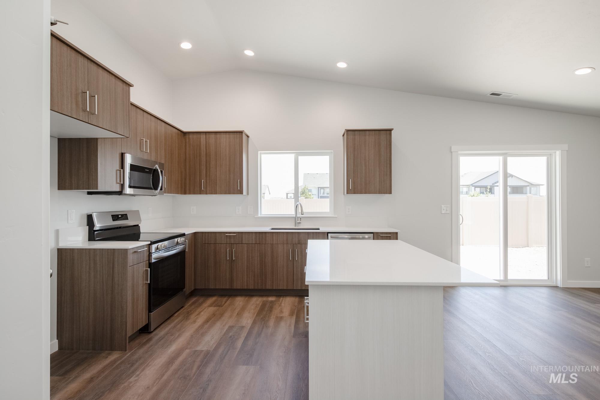 Kitchen featuring stainless steel appliances, vaulted ceiling, modern cabinets, dark wood-style floors, and recessed lighting