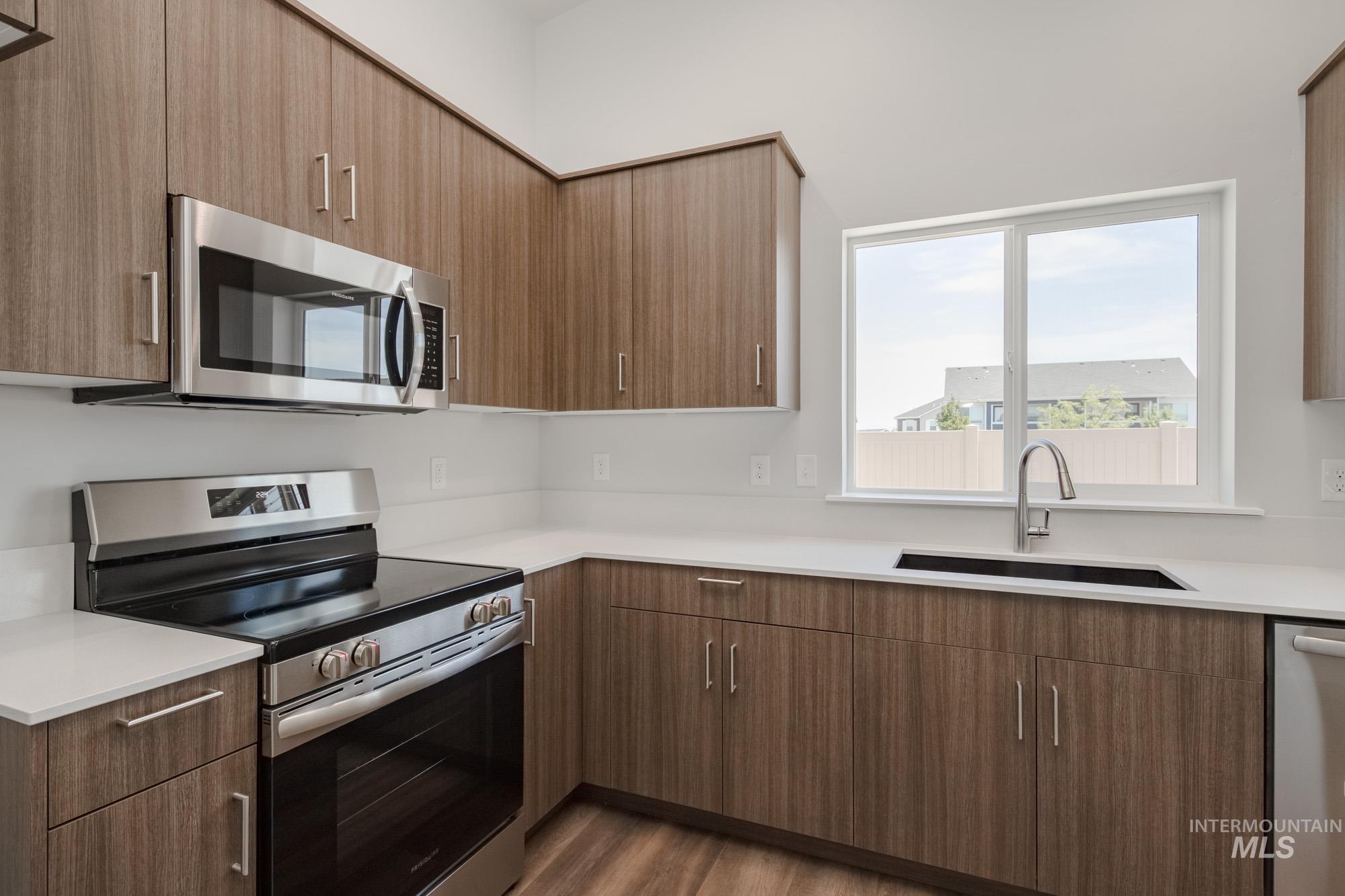 Kitchen with appliances with stainless steel finishes, modern cabinets, dark wood finished floors, brown cabinetry, and light stone counters