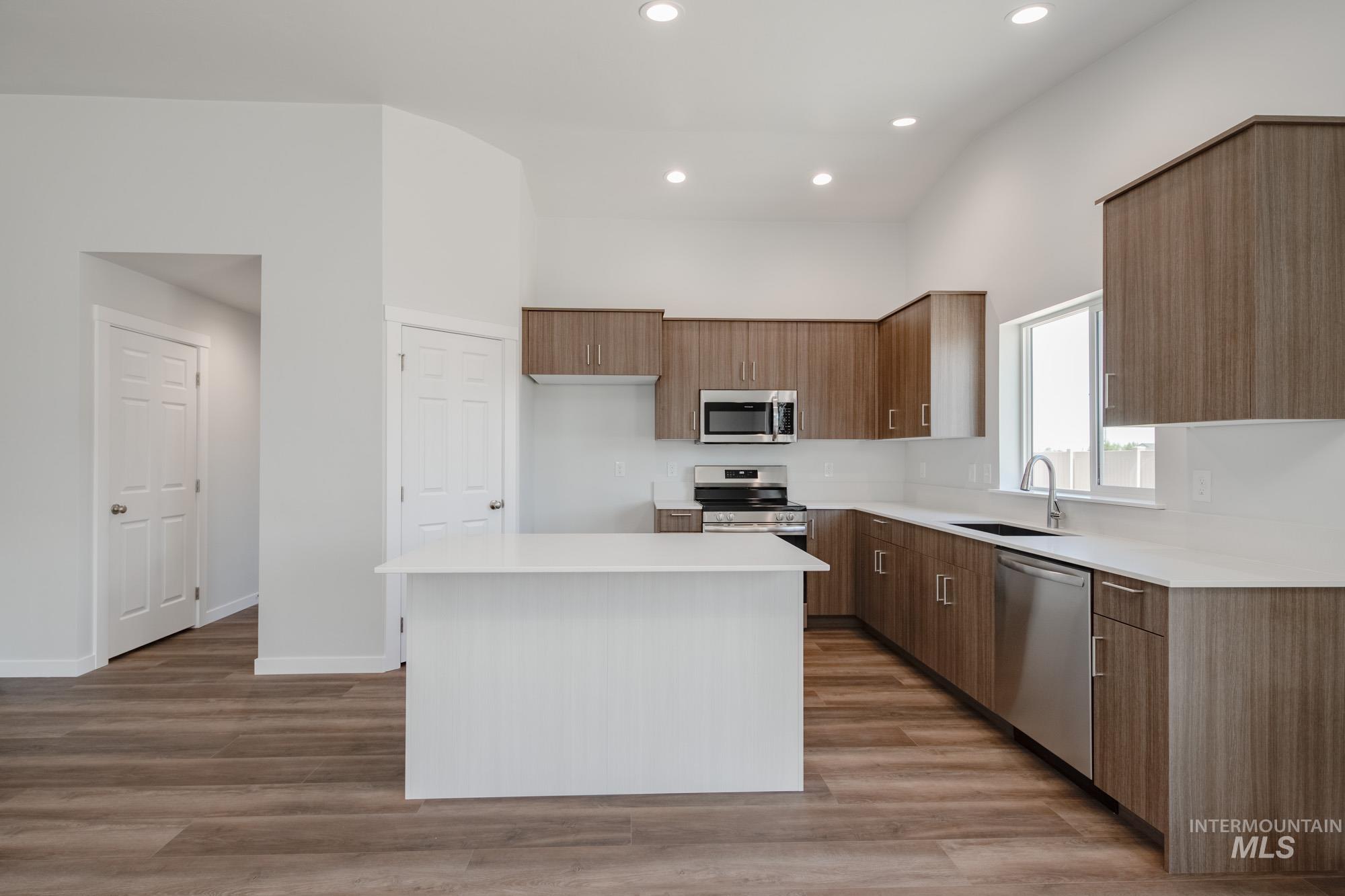 Kitchen featuring modern cabinets, brown cabinetry, recessed lighting, appliances with stainless steel finishes, and a kitchen island