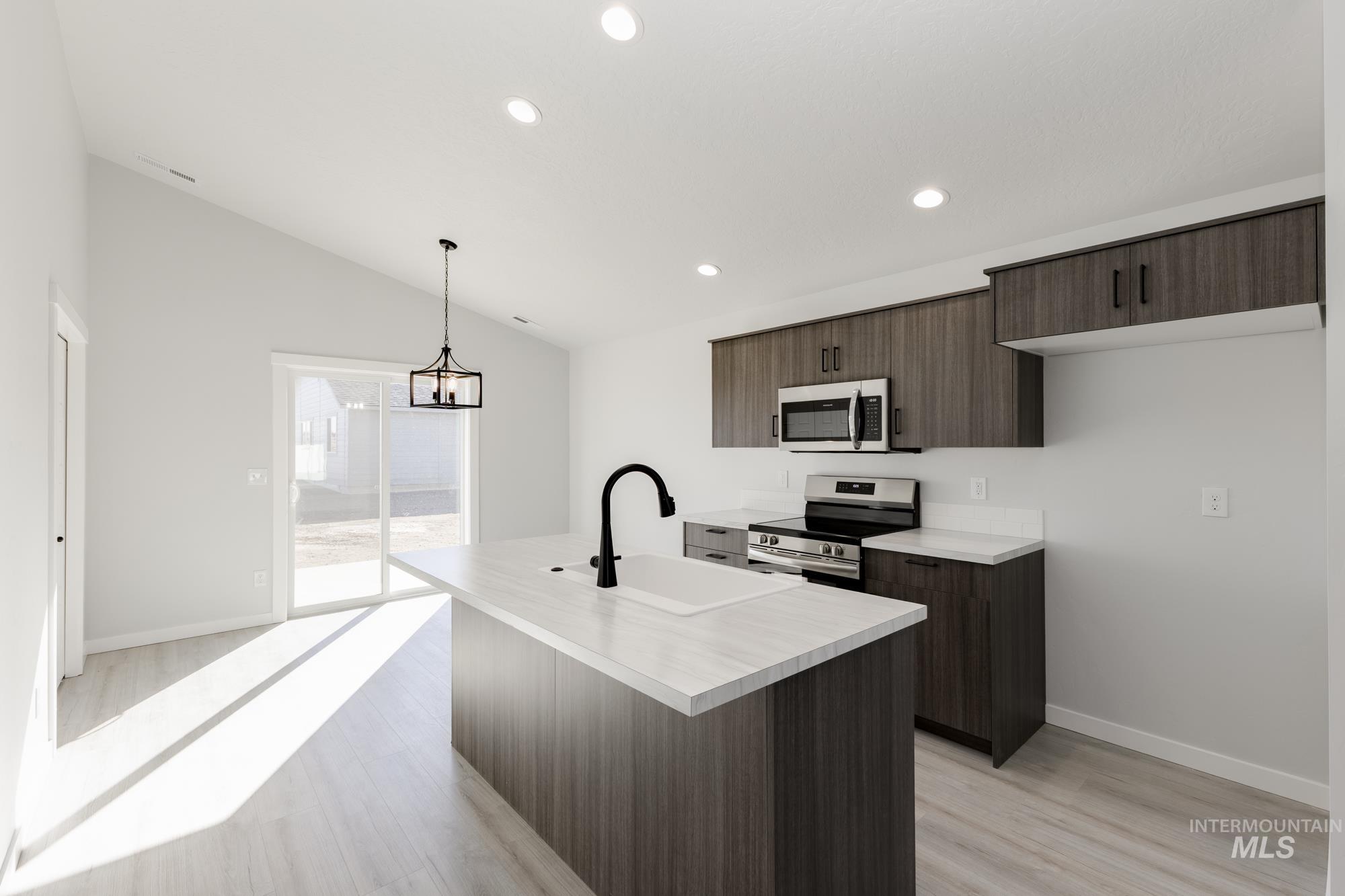 Kitchen with light countertops, dark brown cabinetry, stainless steel appliances, an island with sink, and light wood-style flooring
