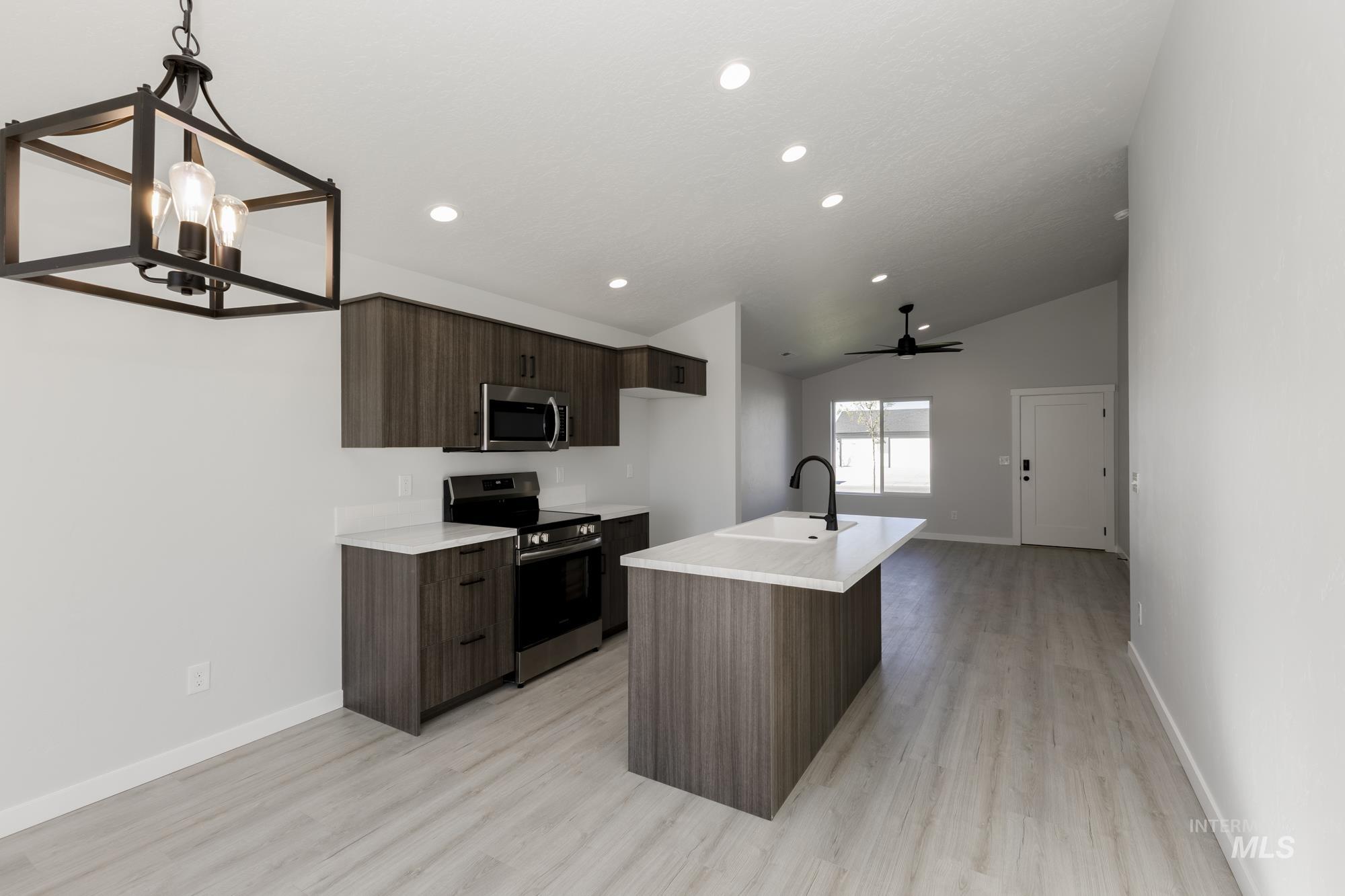 Kitchen with stainless steel appliances, dark brown cabinets, a center island with sink, light wood-style floors, and lofted ceiling