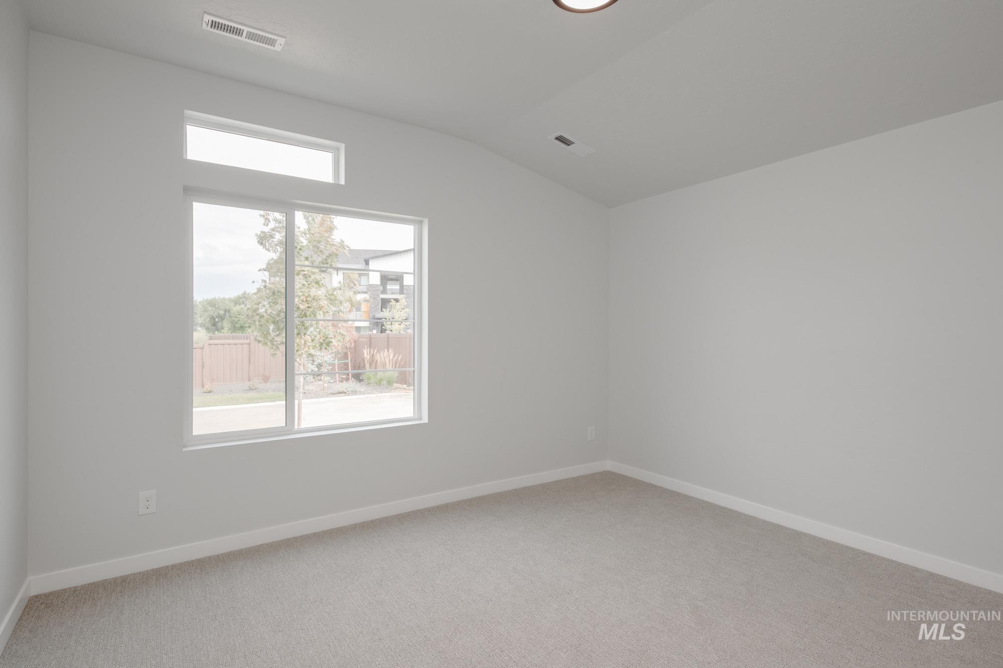 Empty room featuring light carpet and vaulted ceiling