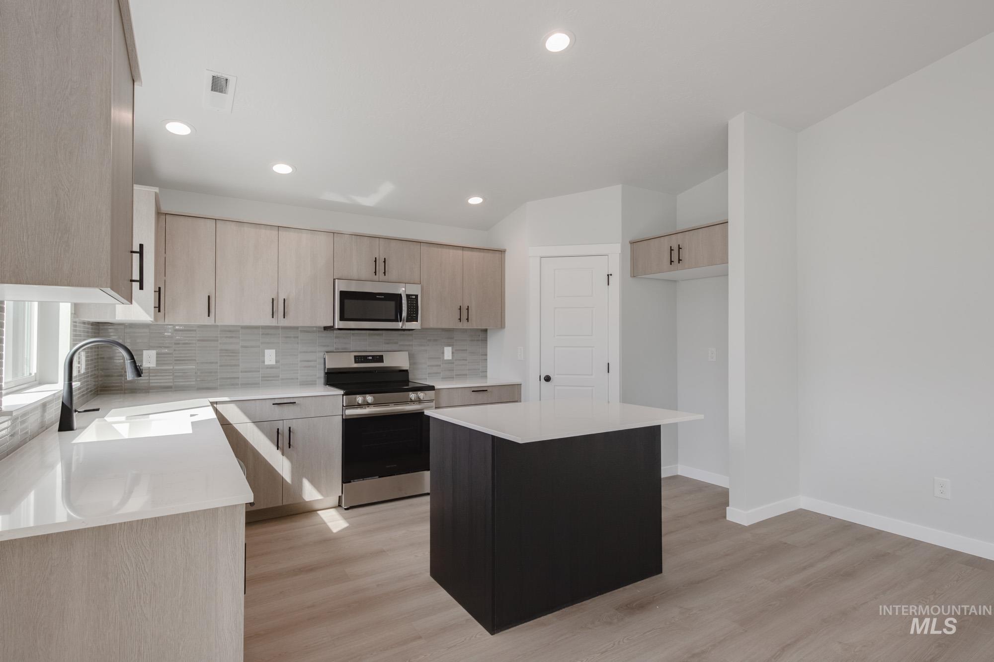 Kitchen with stainless steel appliances, a kitchen island, tasteful backsplash, light stone counters, and recessed lighting