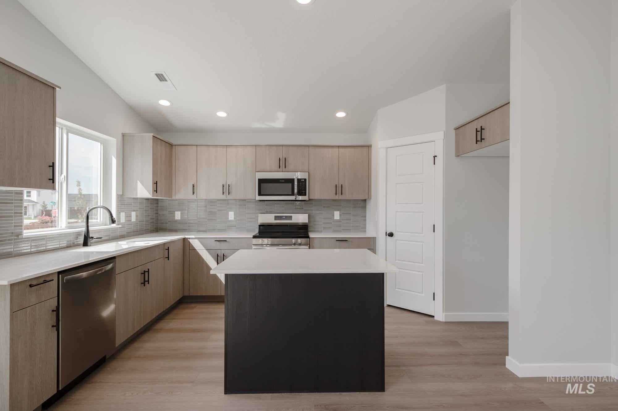 Kitchen with light brown cabinets, a kitchen island, decorative backsplash, stainless steel appliances, and light stone counters
