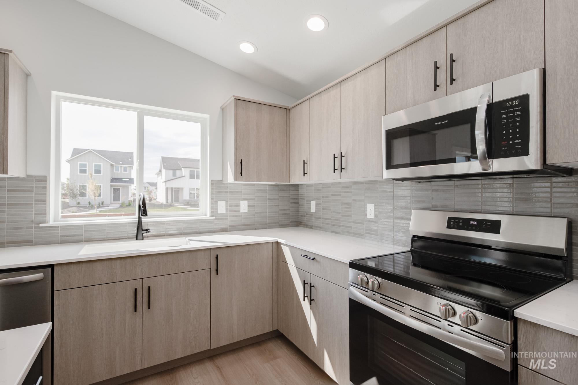 Kitchen with appliances with stainless steel finishes, light brown cabinets, light wood-style floors, decorative backsplash, and recessed lighting
