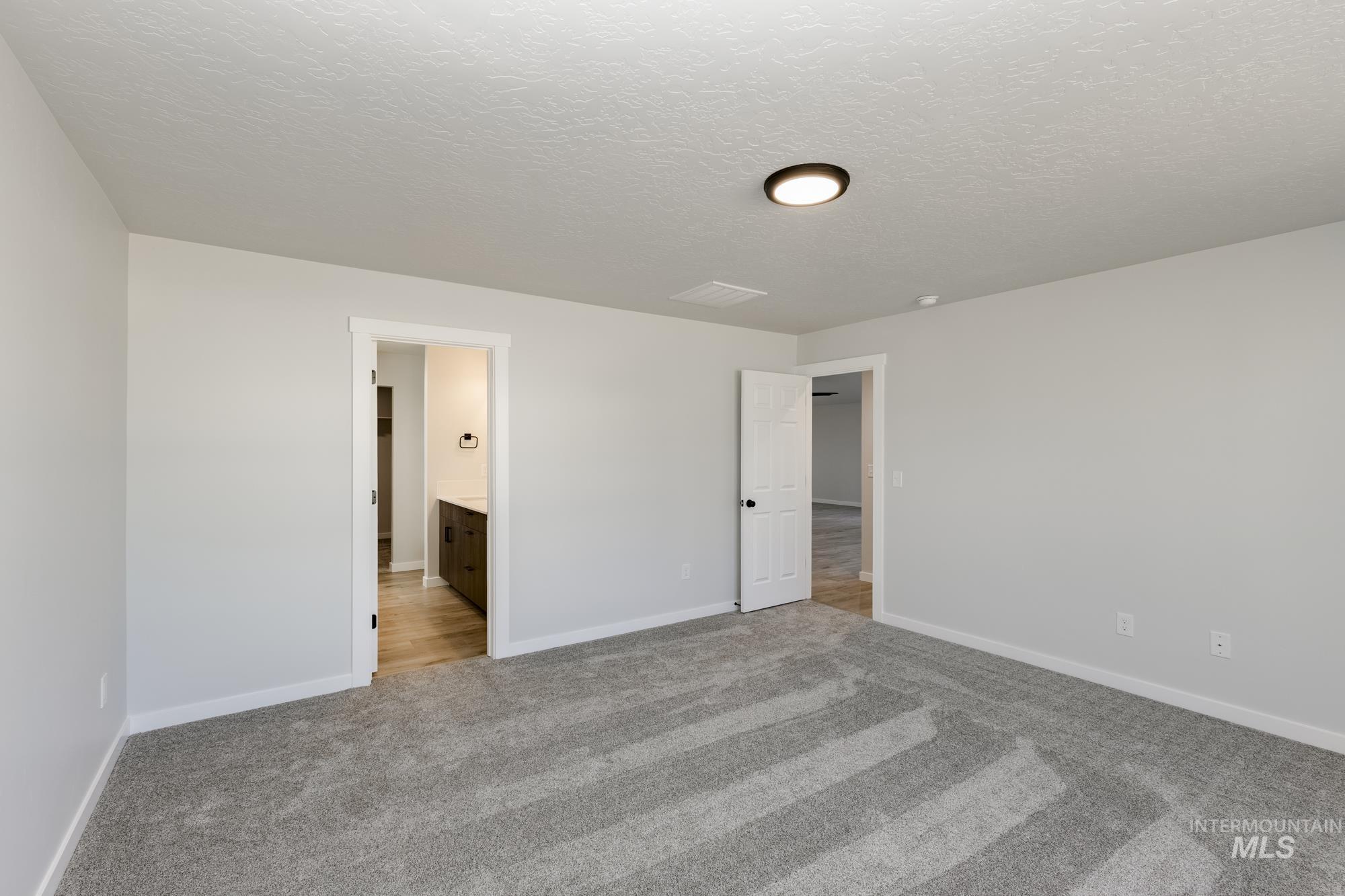 Unfurnished bedroom with light carpet, ensuite bathroom, and a textured ceiling