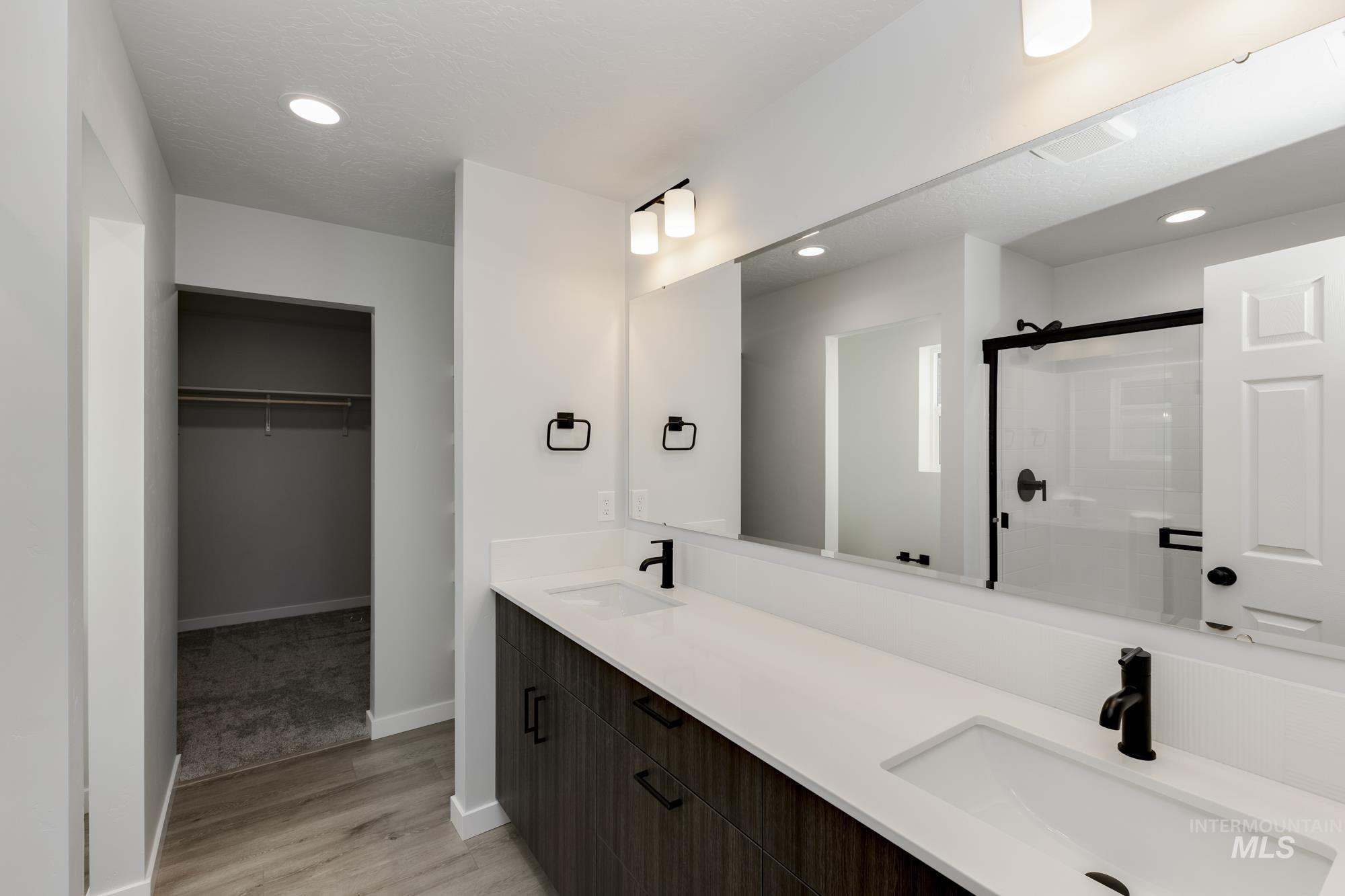 Full bathroom featuring recessed lighting, a spacious closet, double vanity, a stall shower, and light wood-style flooring