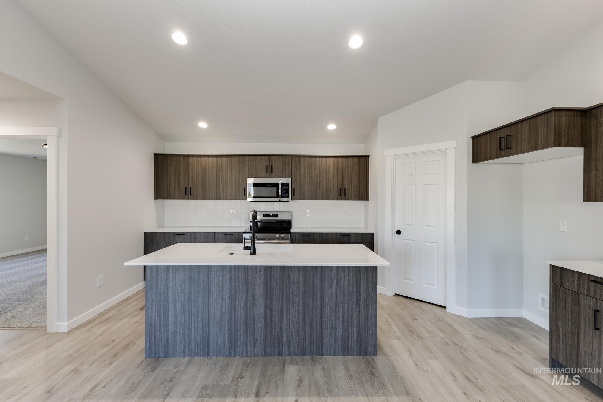 Kitchen featuring modern cabinets, an island with sink, dark brown cabinetry, recessed lighting, and appliances with stainless steel finishes