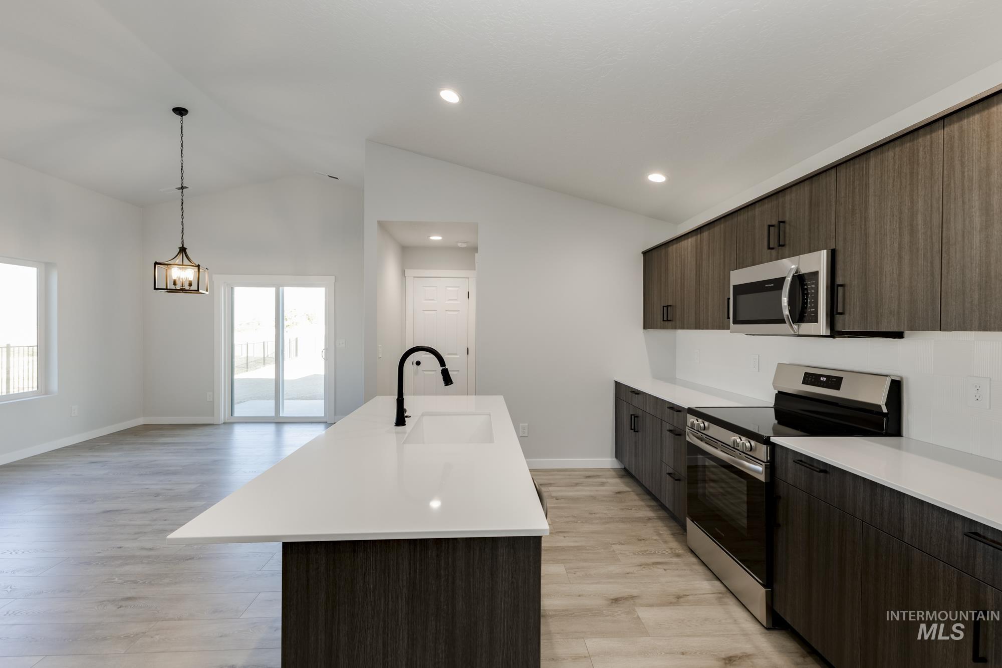 Kitchen featuring stainless steel appliances, lofted ceiling, a center island with sink, dark brown cabinets, and light wood-style floors