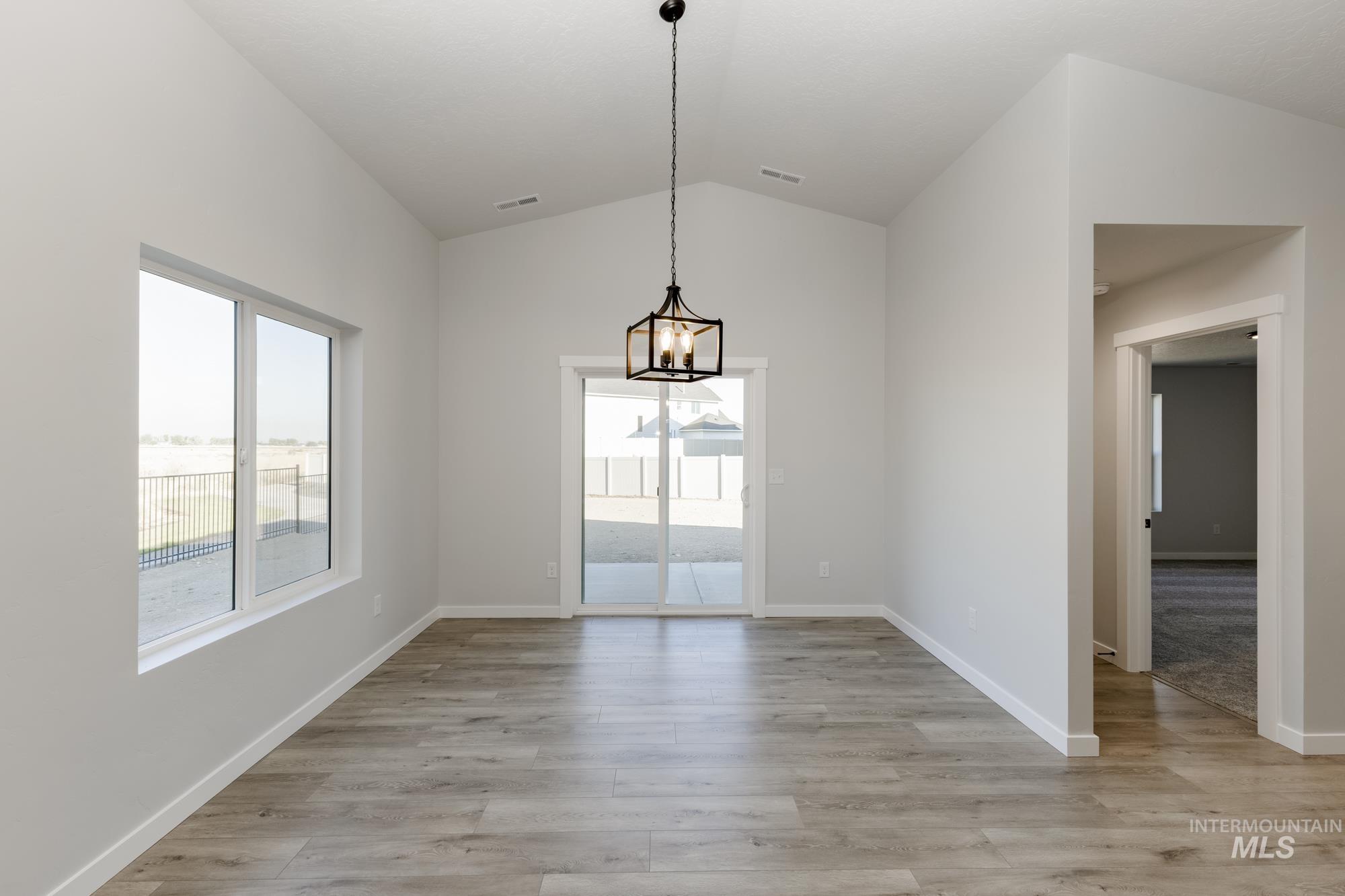 Unfurnished dining area with healthy amount of natural light, light wood-type flooring, lofted ceiling, and a chandelier