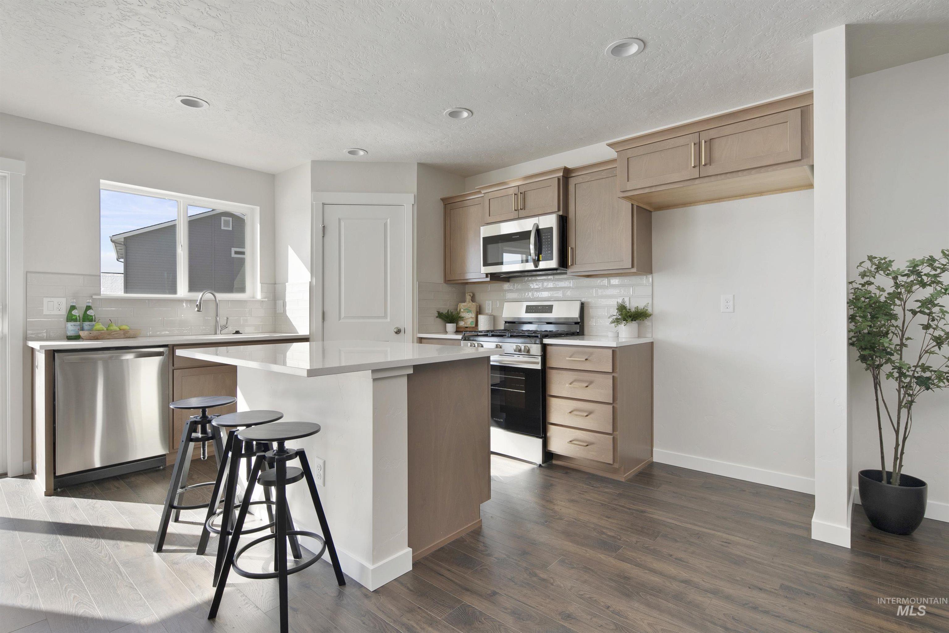 Kitchen featuring stainless steel appliances, a kitchen breakfast bar, tasteful backsplash, dark wood-type flooring, and a textured ceiling