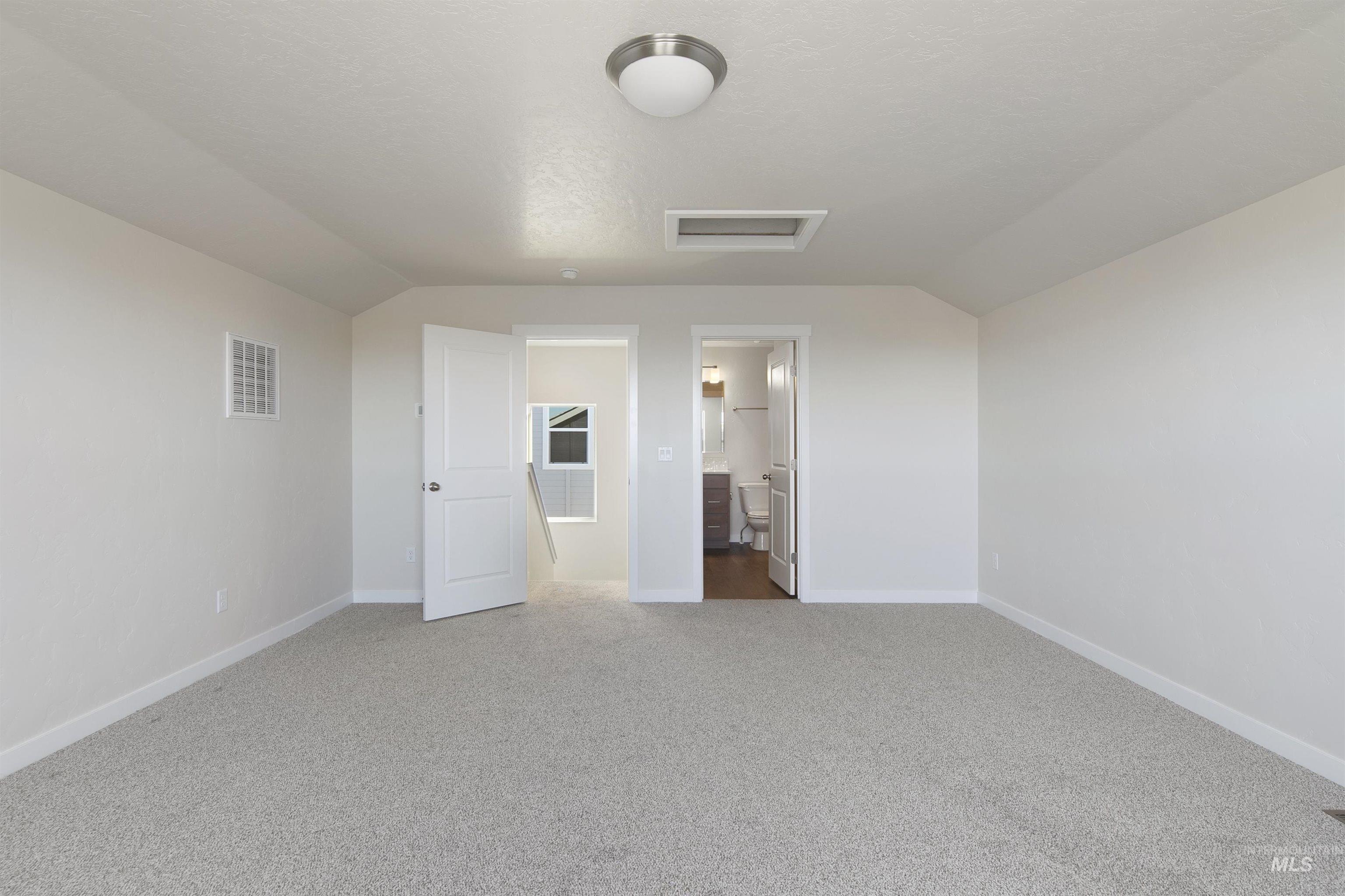 Unfurnished bedroom featuring vaulted ceiling, light carpet, ensuite bathroom, a textured ceiling, and attic access