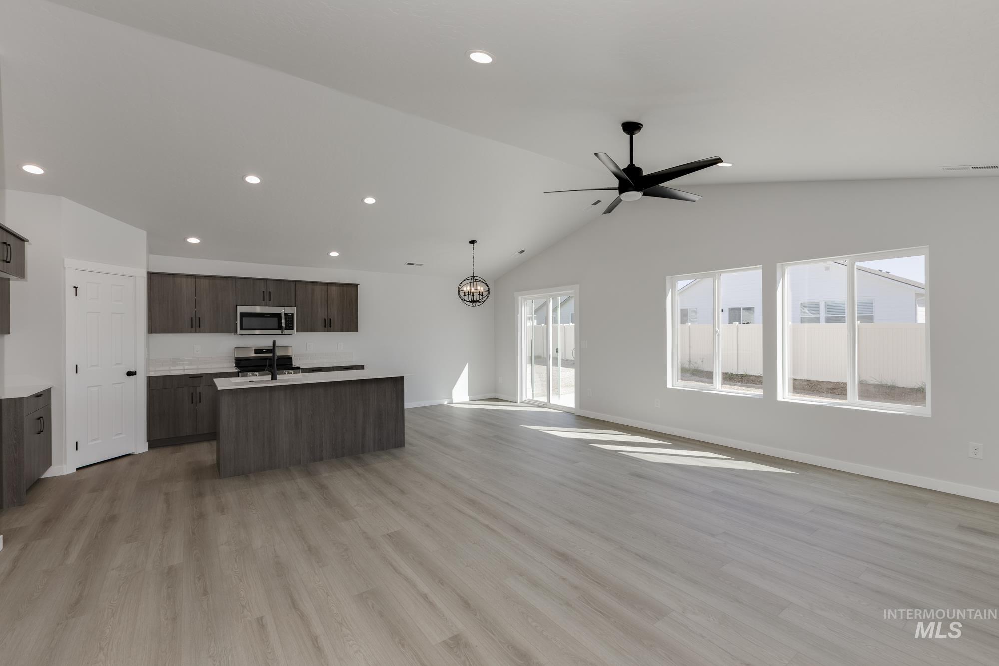 Kitchen featuring open floor plan, an island with sink, light wood finished floors, vaulted ceiling, and appliances with stainless steel finishes
