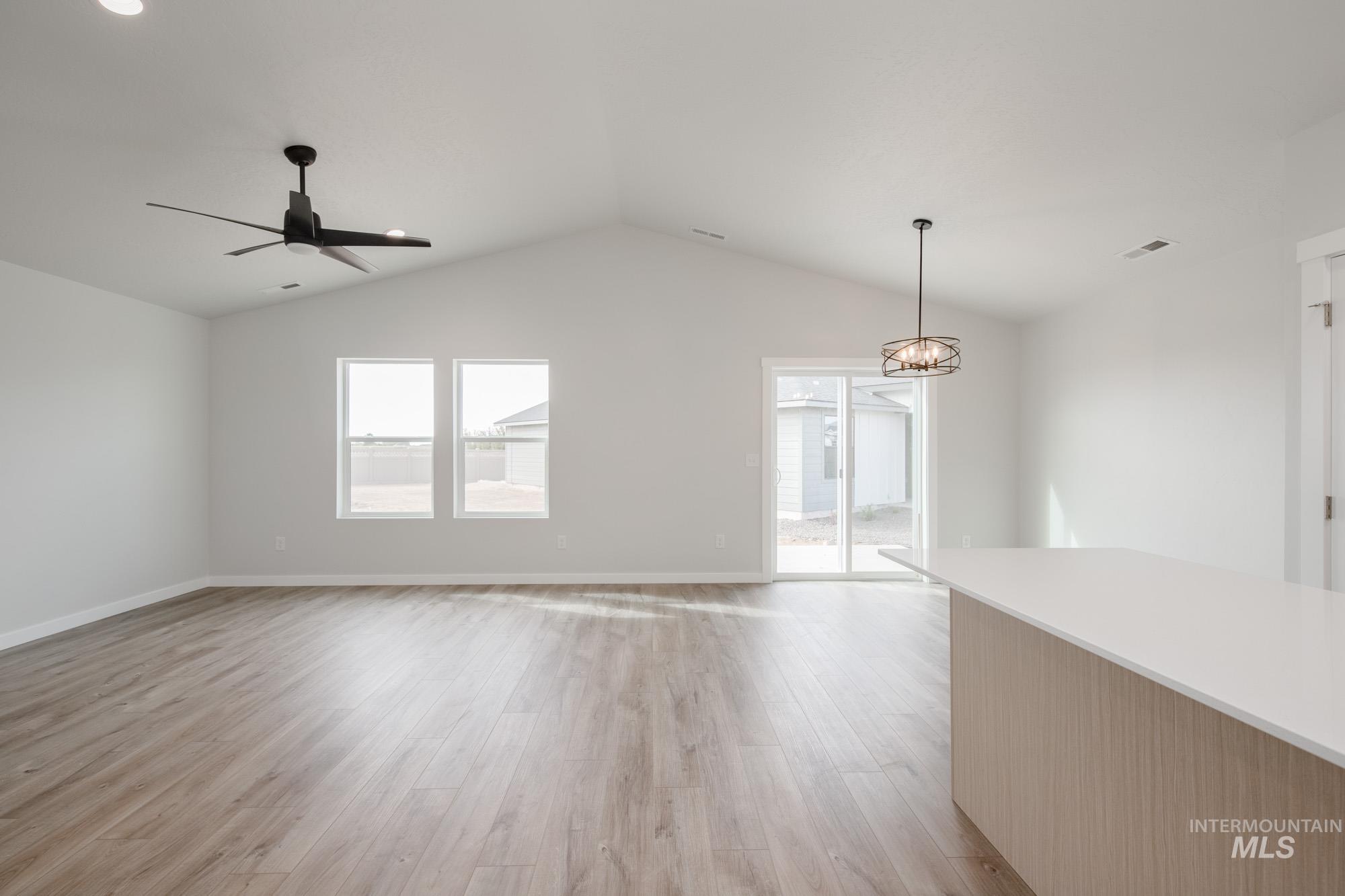Unfurnished living room with light wood-style floors, lofted ceiling, a ceiling fan, and a chandelier