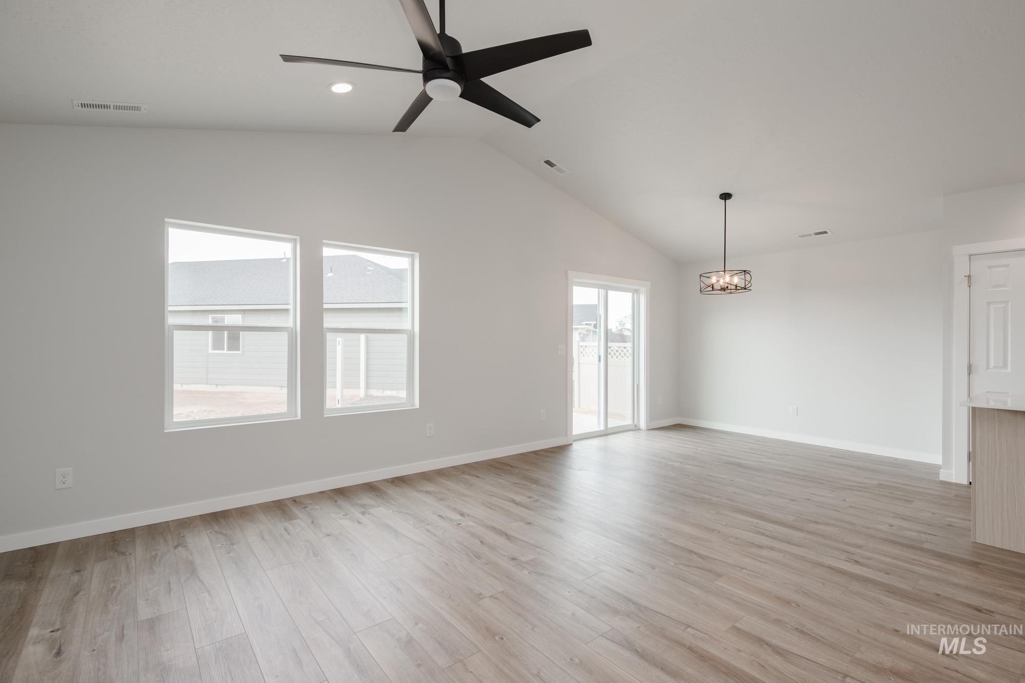 Unfurnished room with light wood finished floors, lofted ceiling, ceiling fan, and a chandelier