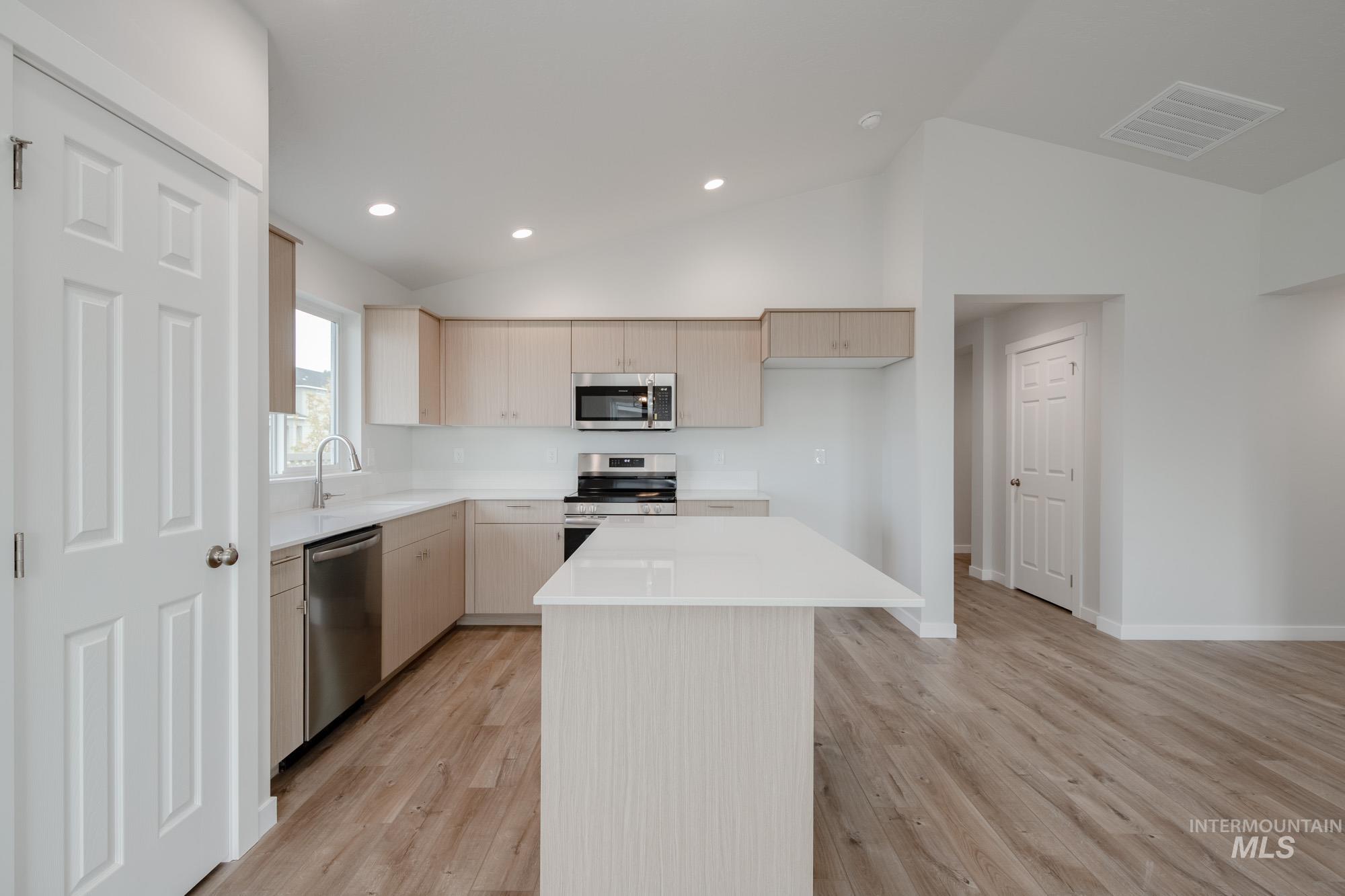 Kitchen featuring a kitchen island, appliances with stainless steel finishes, recessed lighting, light wood-style floors, and lofted ceiling