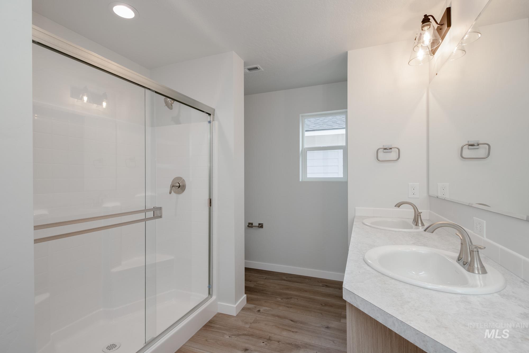 Full bath featuring light wood-style flooring, a stall shower, double vanity, and recessed lighting