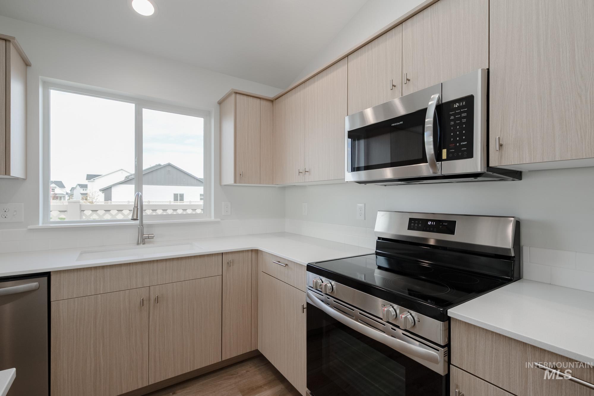 Kitchen with stainless steel appliances, light brown cabinets, wood finished floors, recessed lighting, and light stone countertops