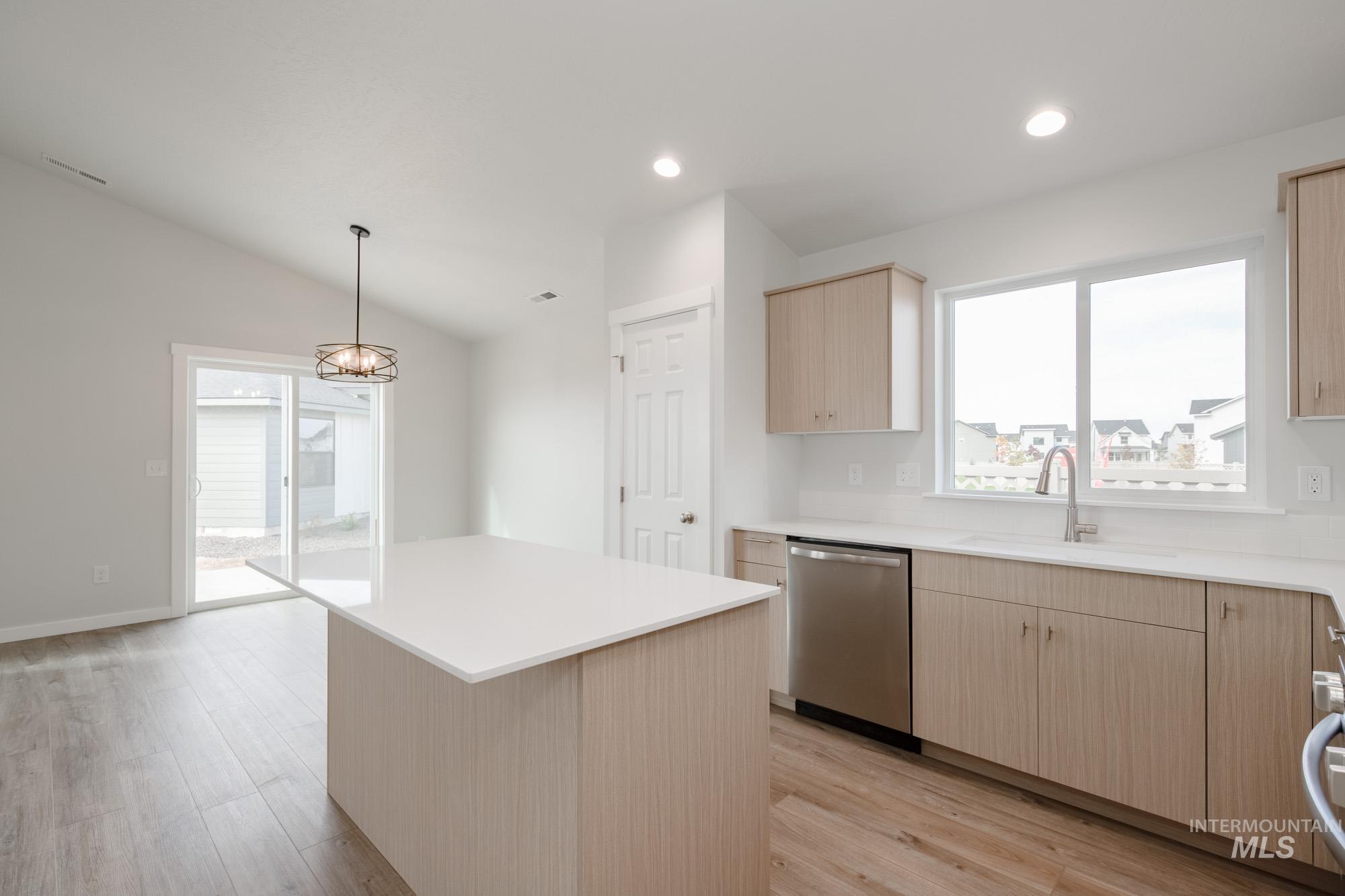 Kitchen with light brown cabinets, a kitchen island, dishwasher, light wood-style flooring, and lofted ceiling