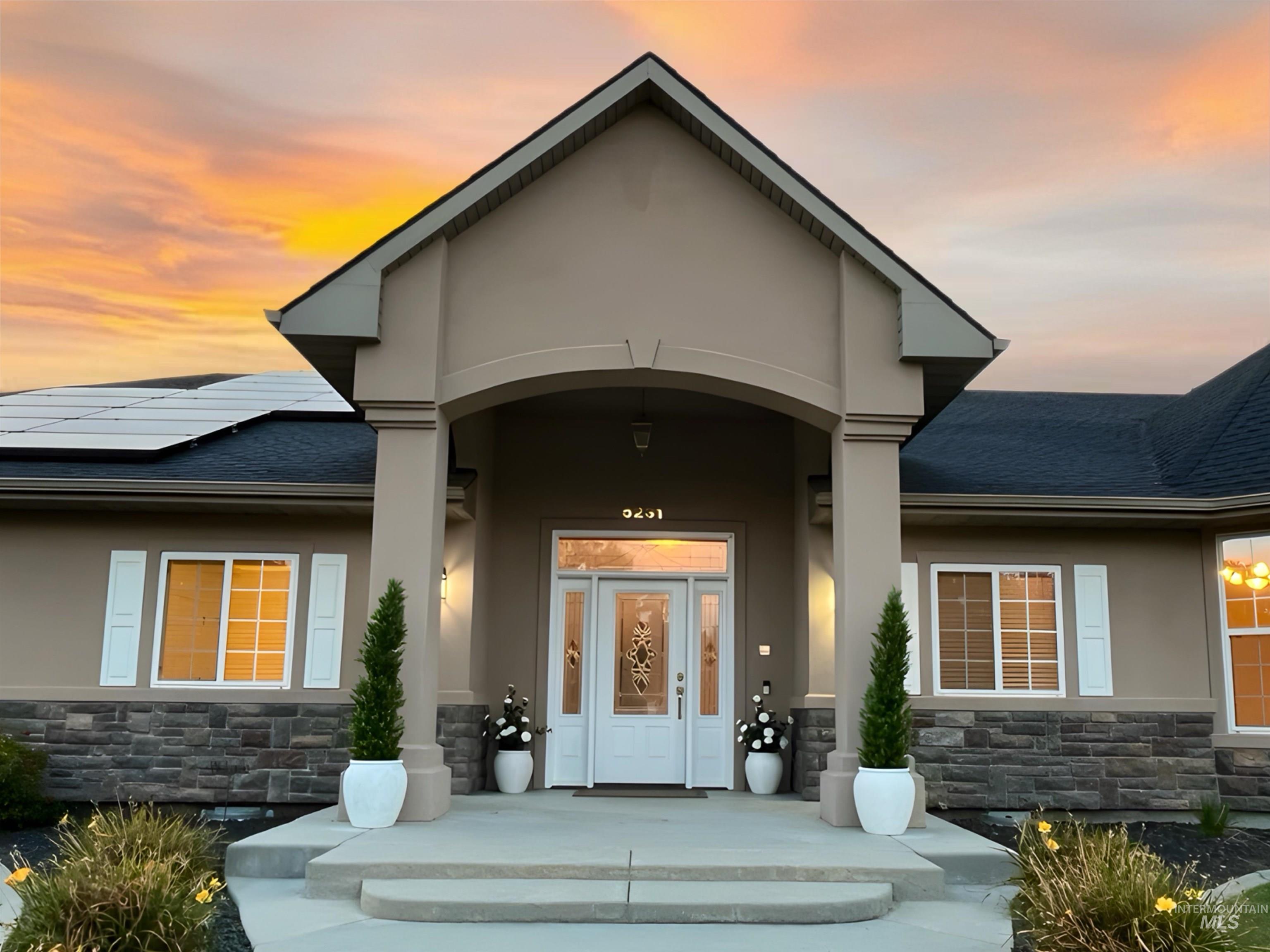 View of exterior entry featuring stone siding, stucco siding, roof with shingles, and roof mounted solar panels