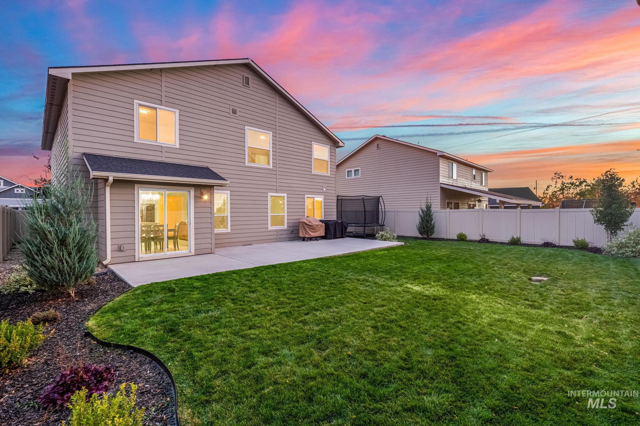 Back of property at dusk with a trampoline, a patio, and a fenced backyard