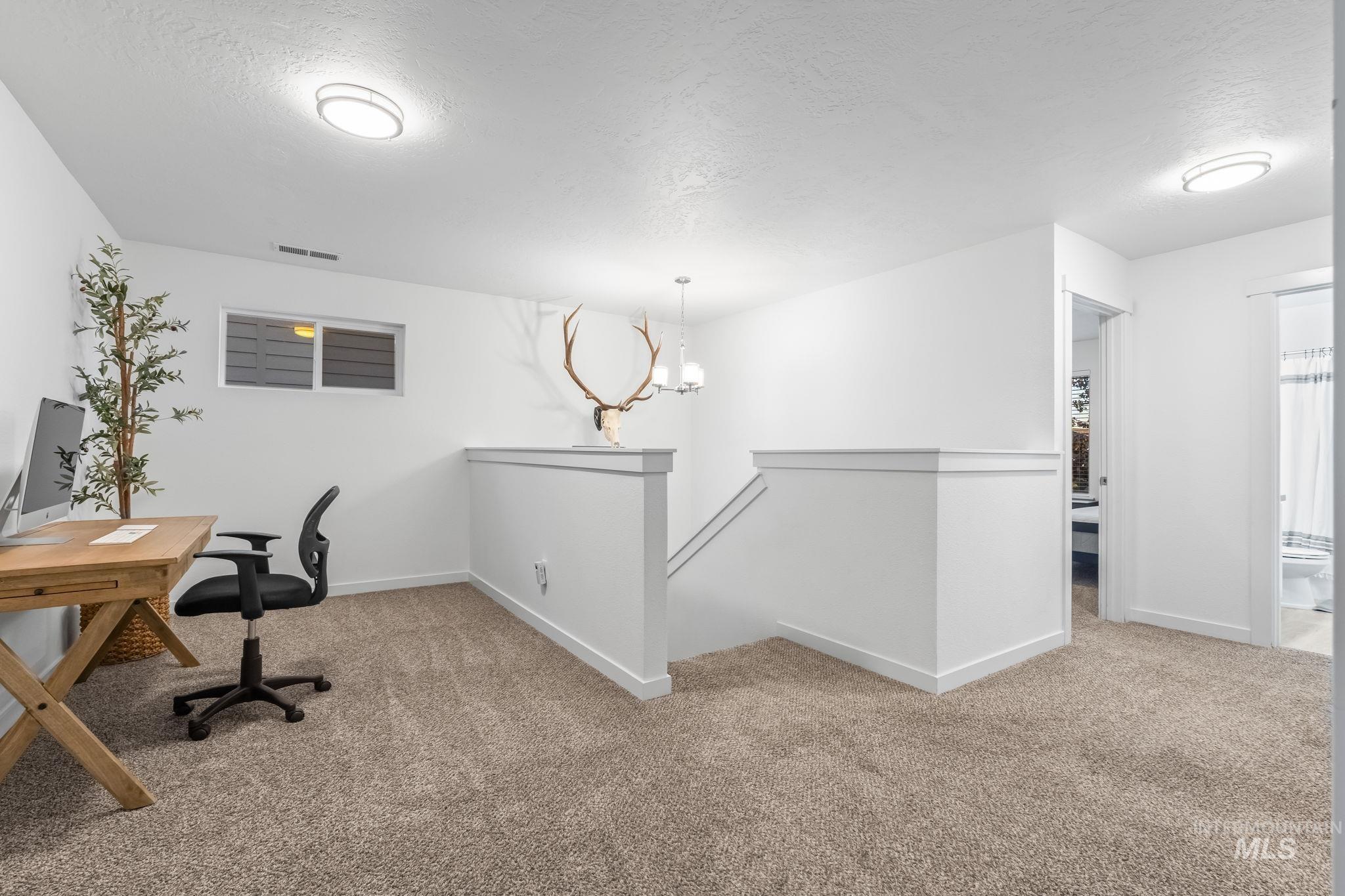 Home office with light colored carpet, a textured ceiling, and a chandelier