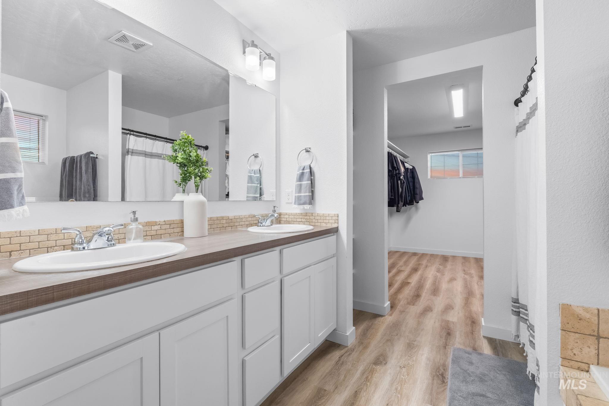 Bathroom with a shower with curtain, double vanity, light wood-type flooring, and a walk in closet