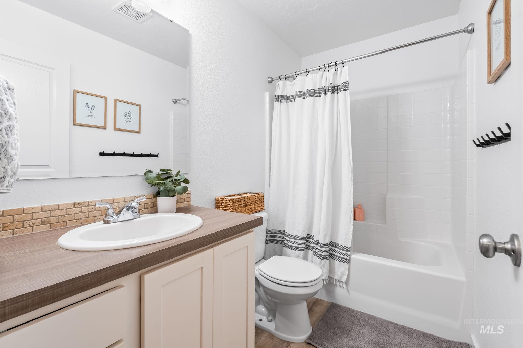 Full bath featuring shower / bath combo, vanity, and tasteful backsplash
