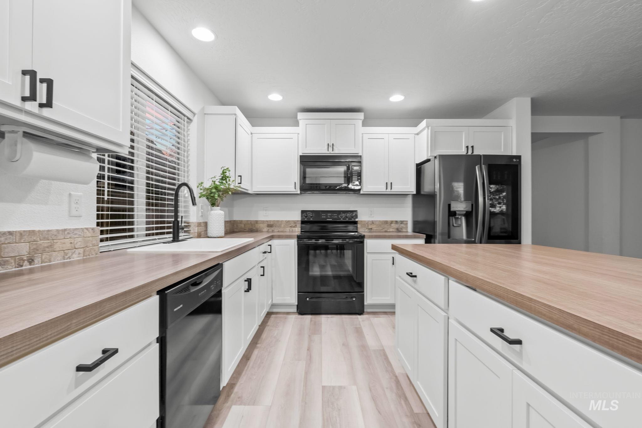 Kitchen with wooden counters, black appliances, white cabinetry, light wood finished floors, and recessed lighting