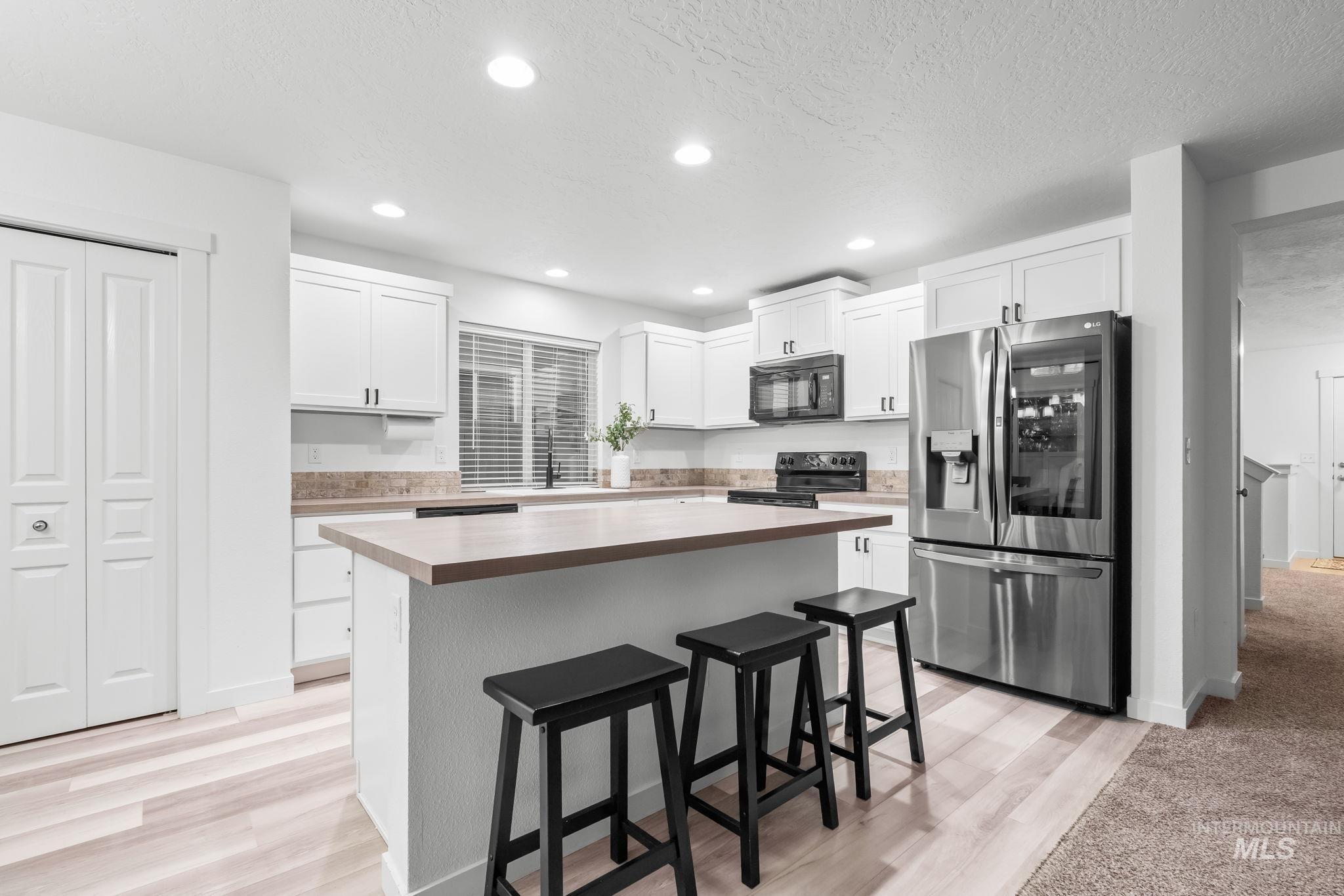 Kitchen featuring a kitchen bar, black appliances, white cabinets, a kitchen island, and a textured ceiling