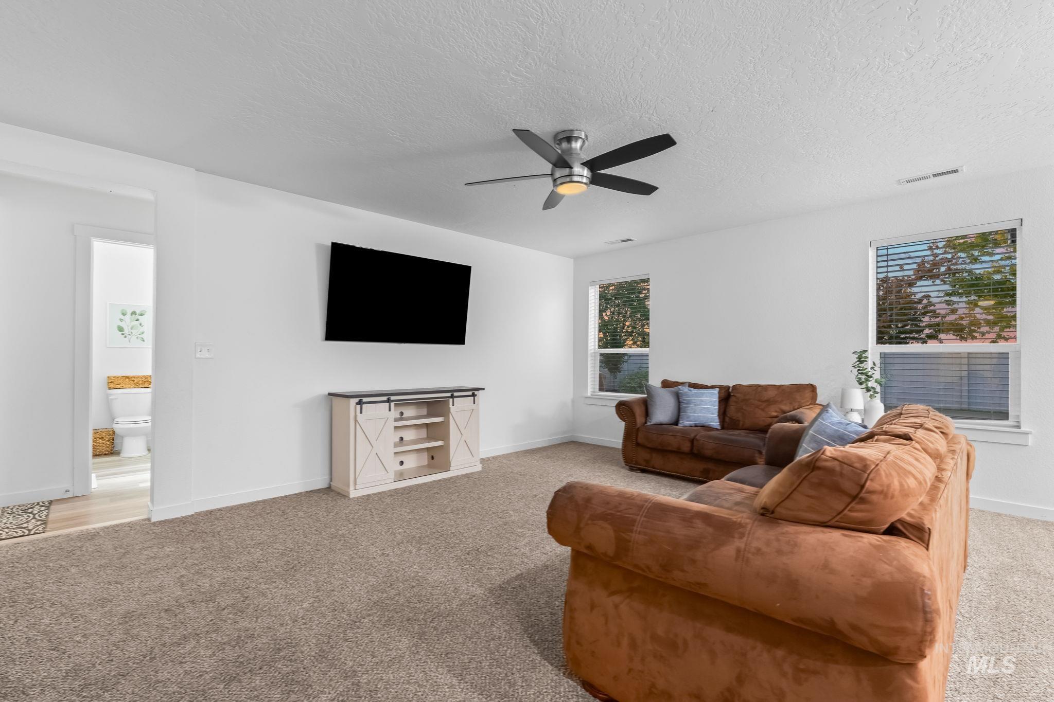 Living area with light carpet, a textured ceiling, and a ceiling fan