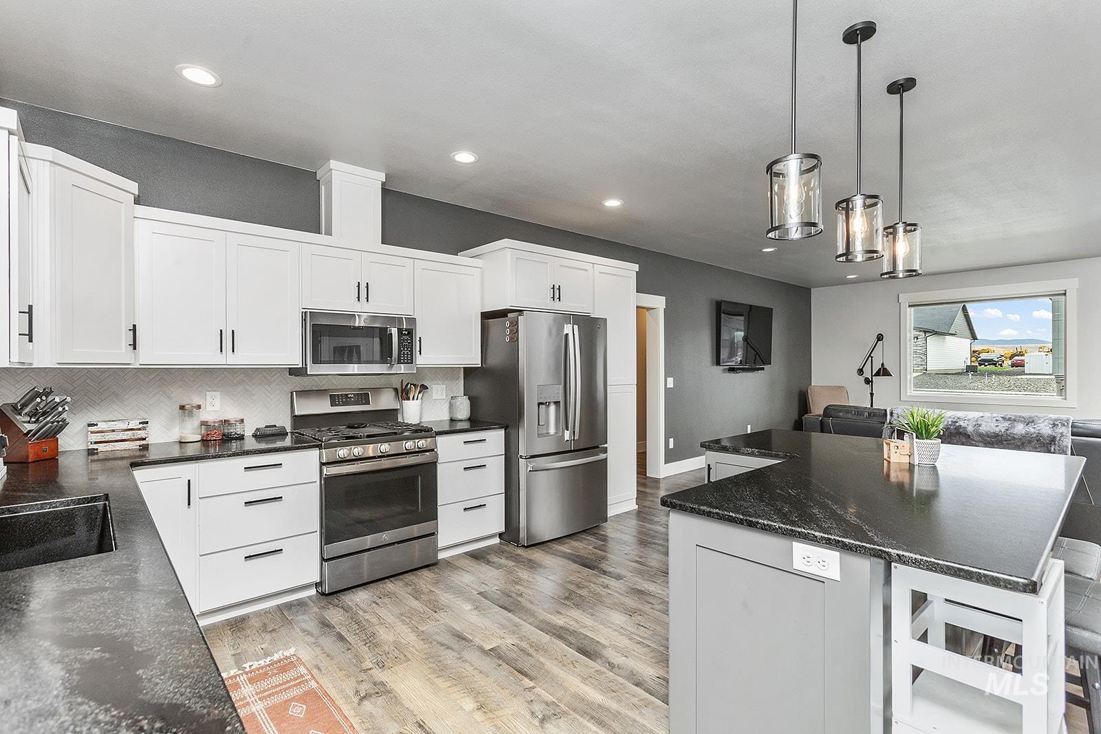 Kitchen featuring stainless steel appliances, pendant lighting, white cabinetry, decorative backsplash, and recessed lighting